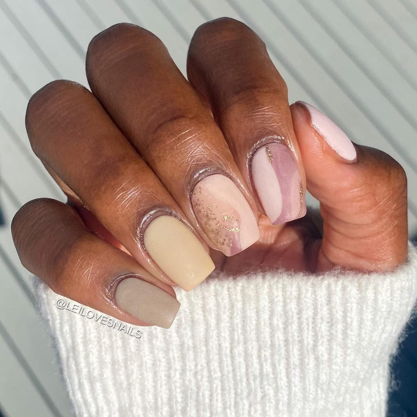 Hand with medium brown skin wearing beige and nude matte solid nails with subtle gold foil accents.