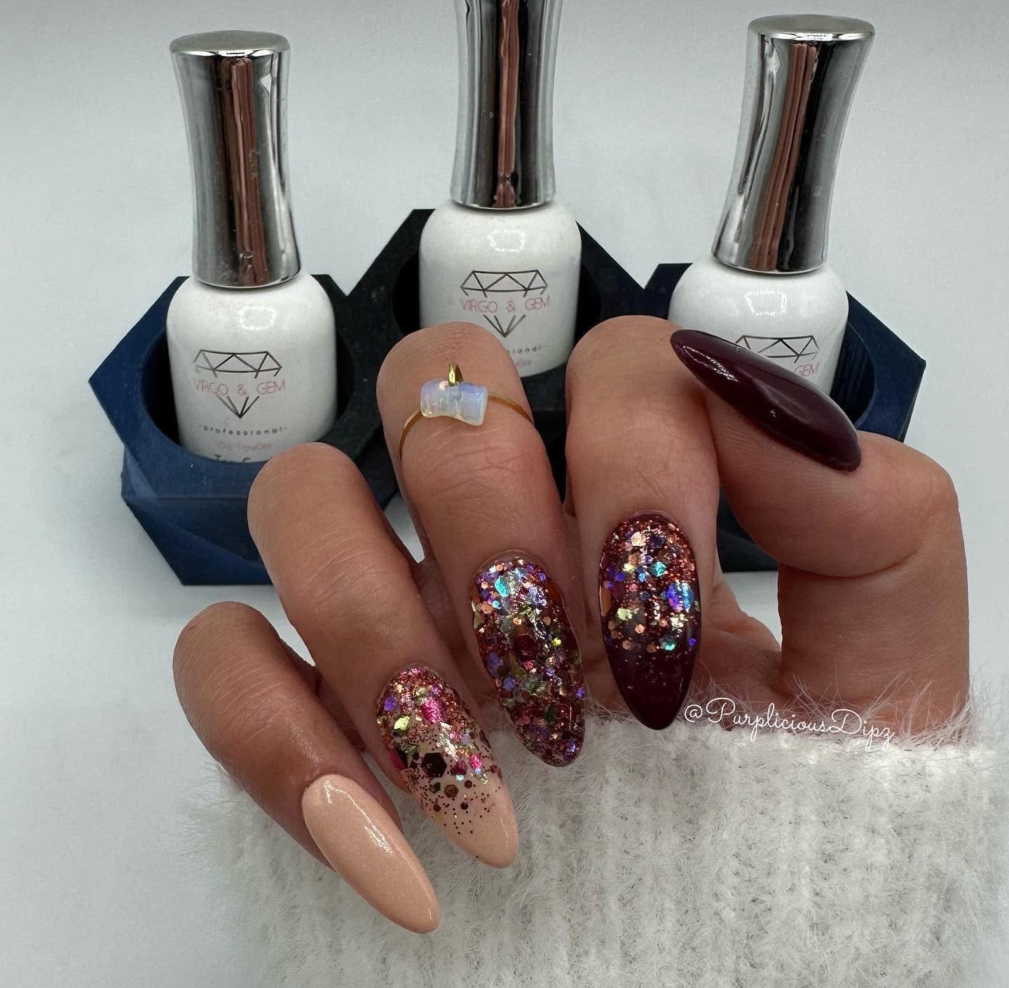 Hand with long almond-shaped nails in beige, nude, dark burgundy, and glittery multicolor polish holding three chrome-capped .
