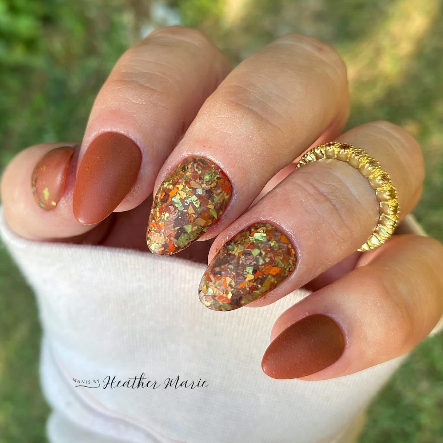 Matte warm brown nails with amber and gold flake accent on almond-shaped tips.