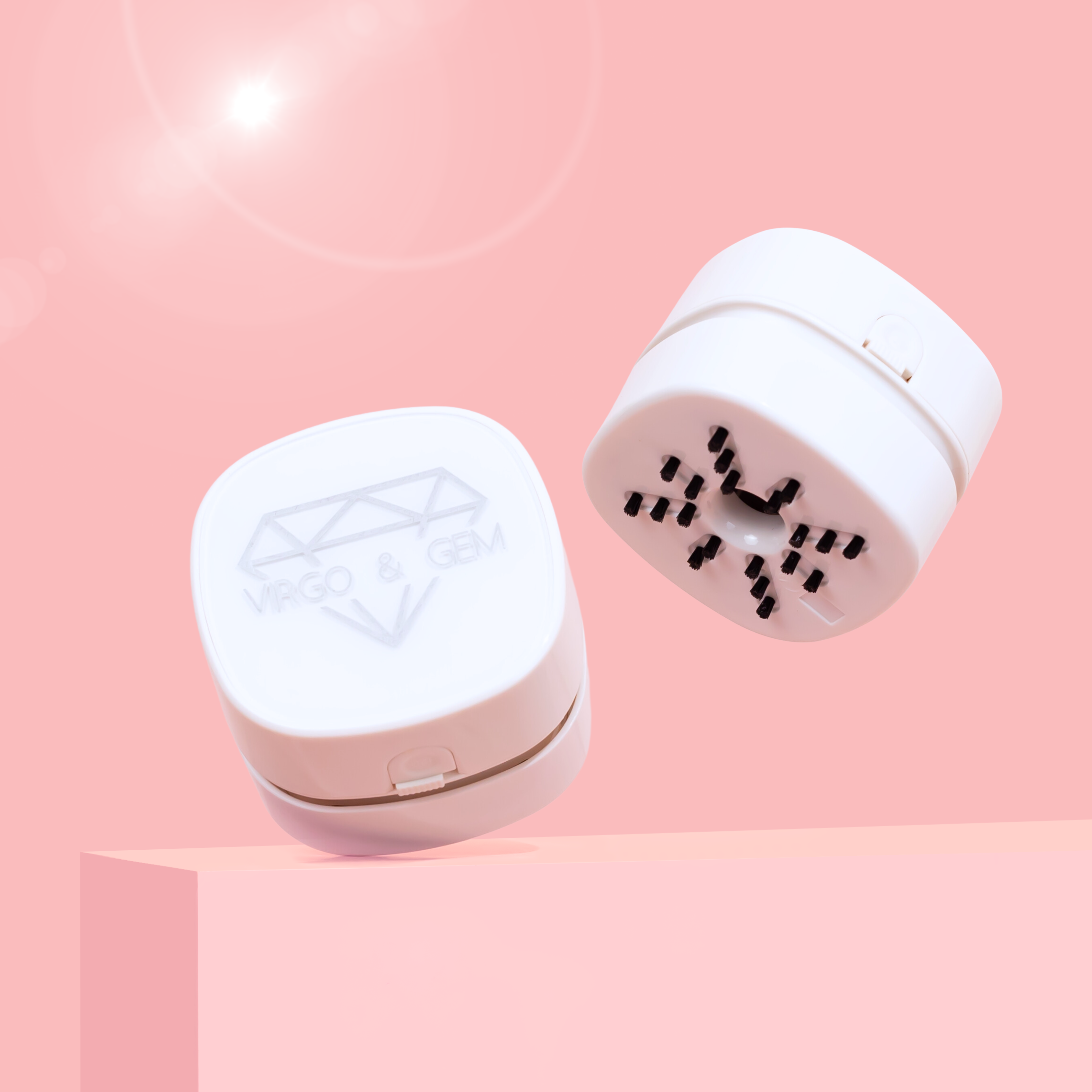 White compact mini desk vacuum with black bristles and geometric logo on top against pink background.