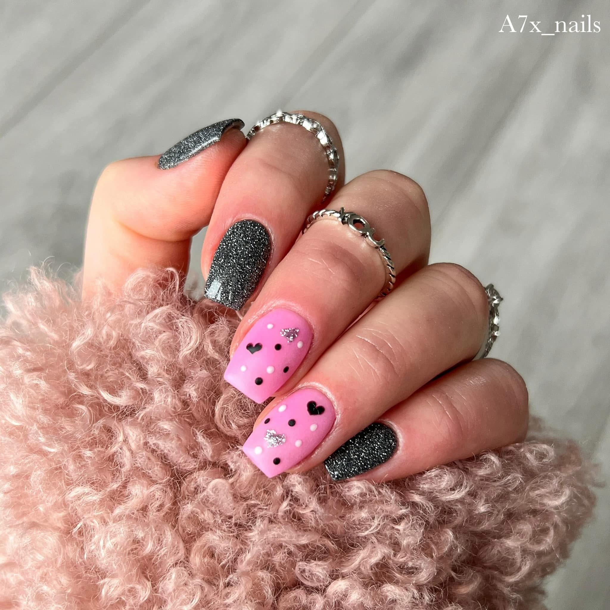 Black fine glitter dip powder nails with reflective silver glitter and pink accent nails with black hearts and dots.
