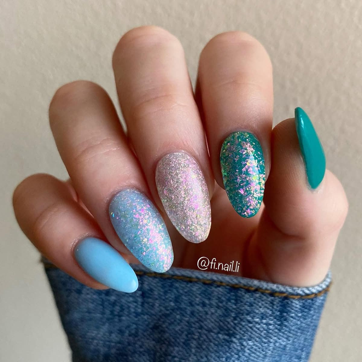 Almond-shaped nails with blue, white, and teal bases featuring iridescent chameleon flake glitter dip powder.