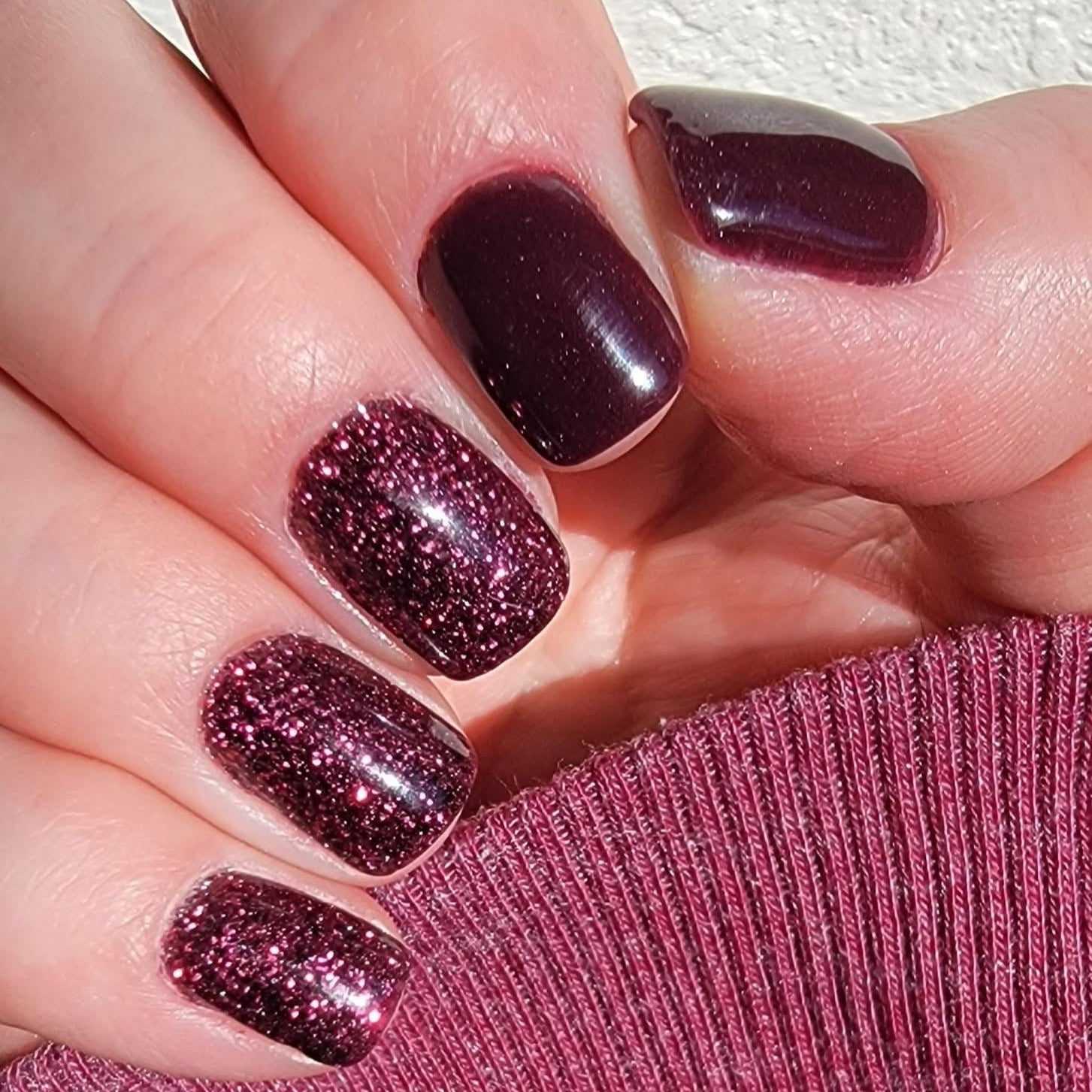 Burgundy glitter dip powder nails with fine shimmer on medium-length rounded tips and textured sweater background.