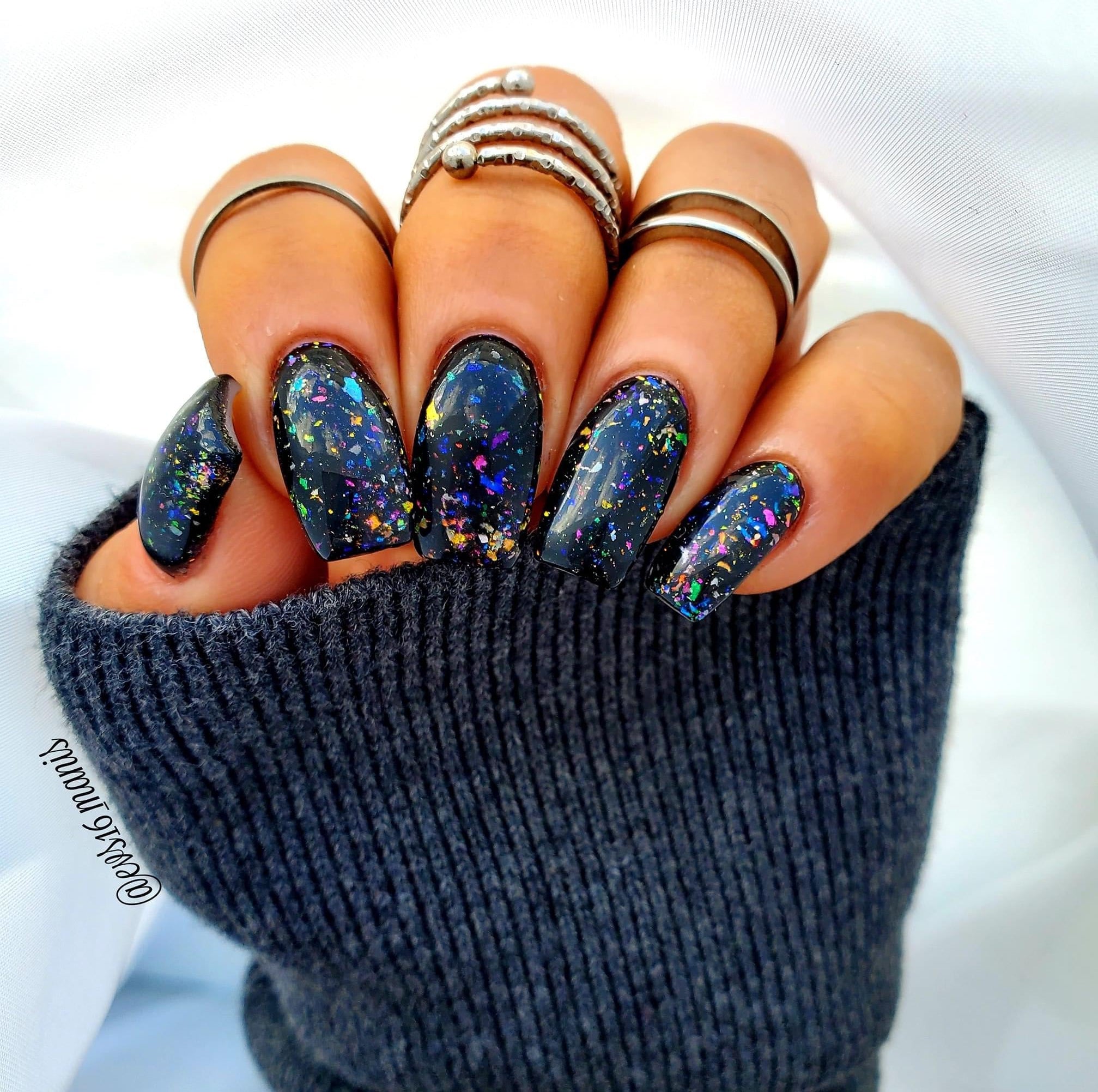 Long almond-shaped nails with black chameleon flake dip powder featuring multicolor, iridescent flakes and subtle sparkle.
