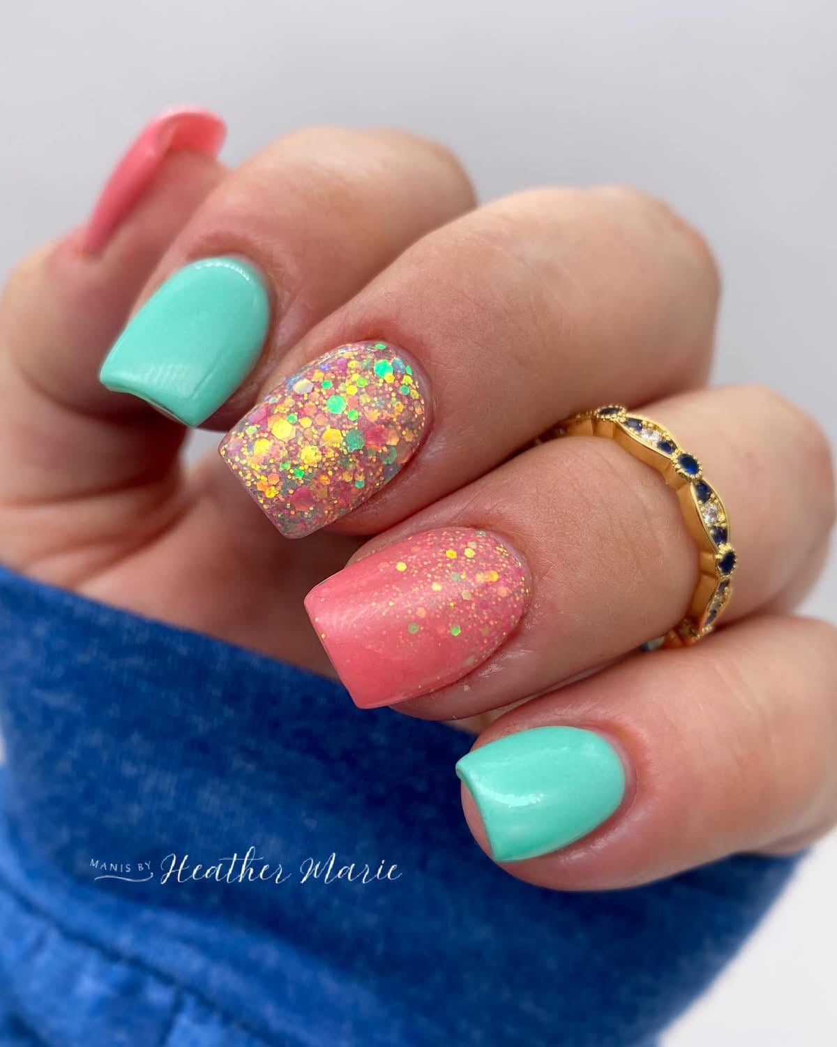 Manicure with alternating mint green and coral pink nails, one coral nail with multicolor glitter, wearing gold ring with.