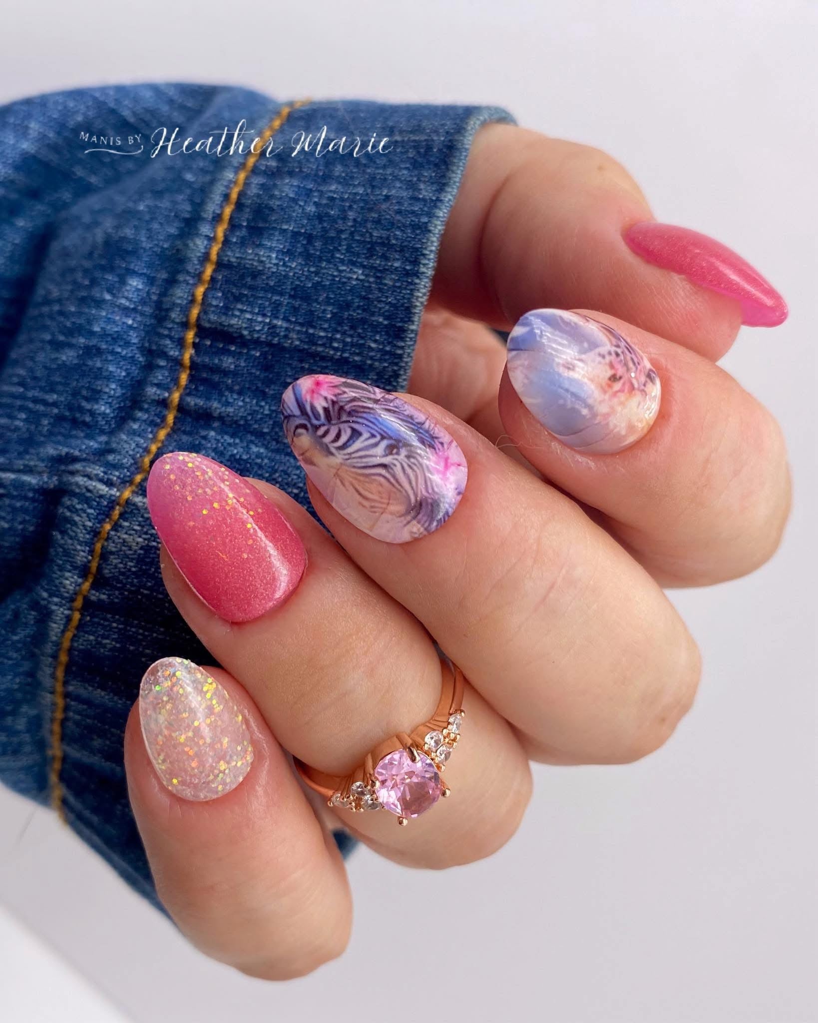 Hand with pink, iridescent white, and fine glitter dip powder nails, floral accent nail, wearing gold ring and denim jacket.
