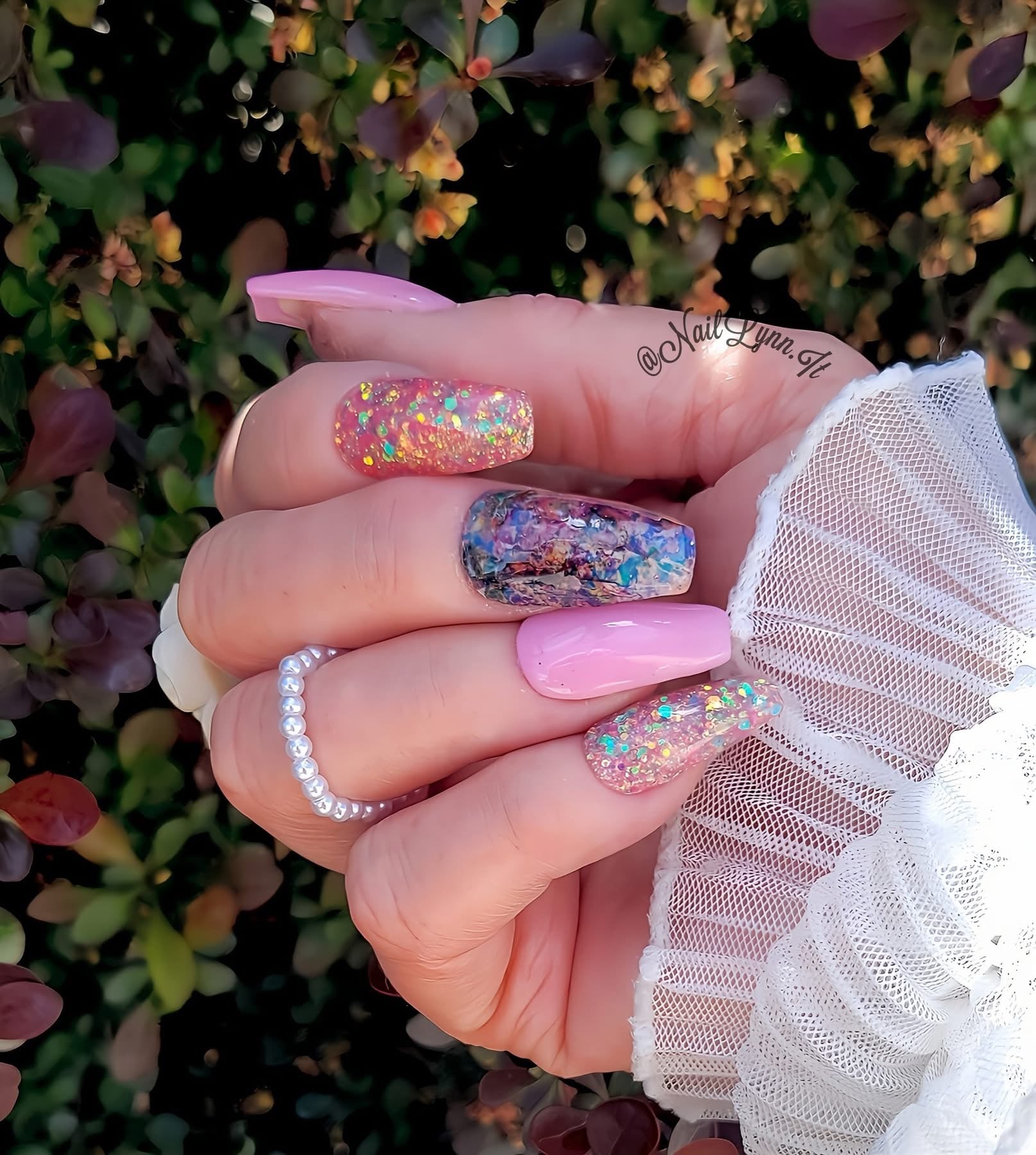 Hand with pink and glittery multicolor chunky glitter nails, including one accent nail with dense multicolor glitter and.