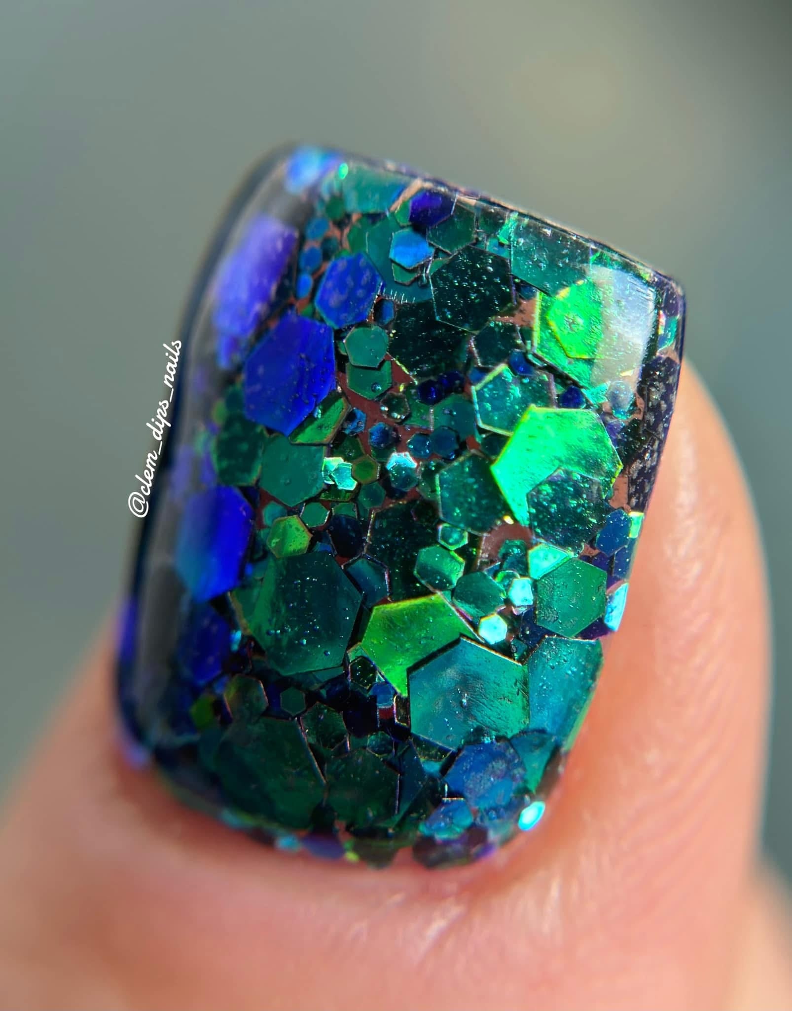 Blue and green chunky glitter dip powder with sparkling hexagonal flakes on nail tip.