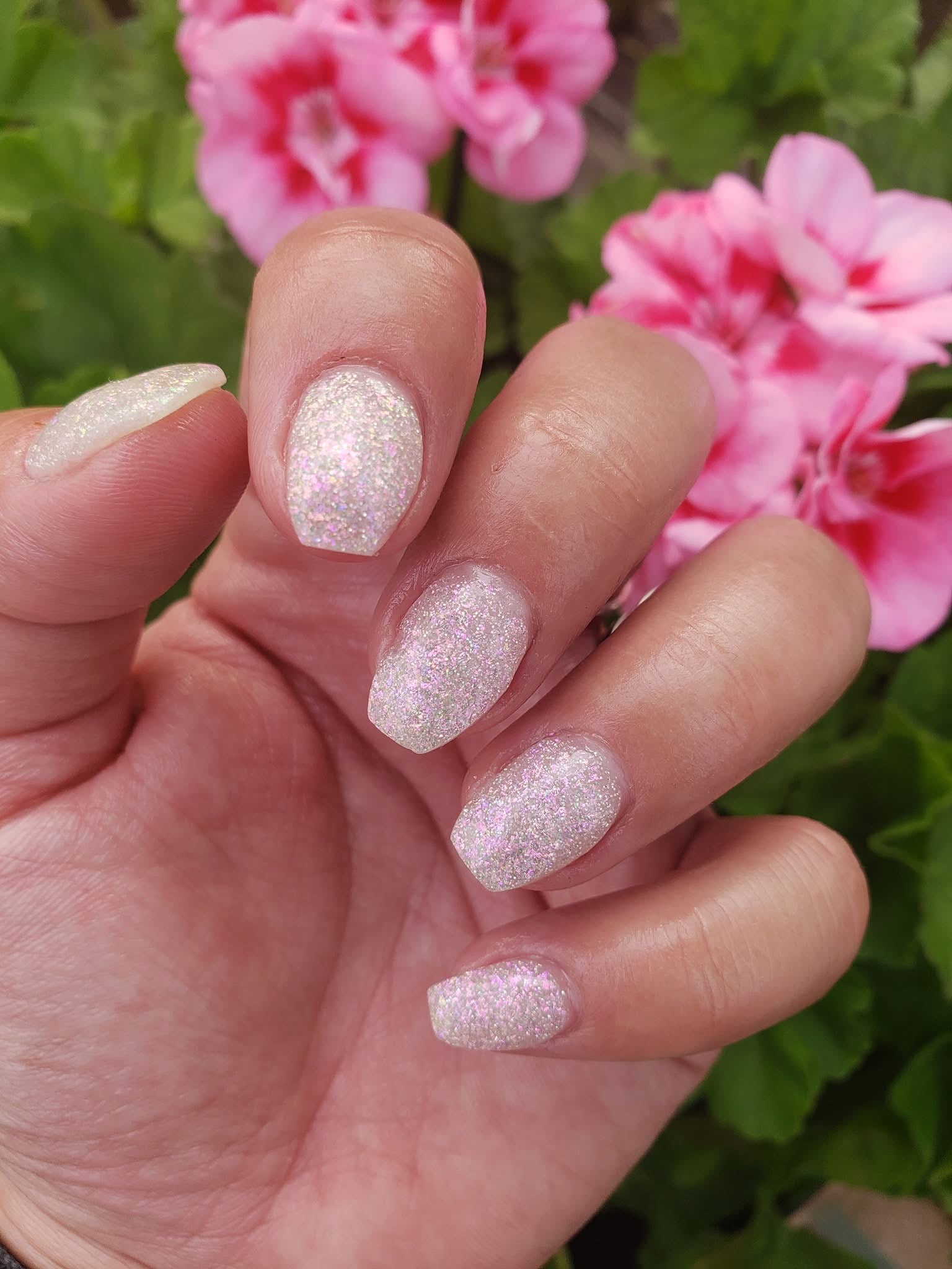 Soft pink nails with white chameleon glitter flakes and a clear dip powder finish.
