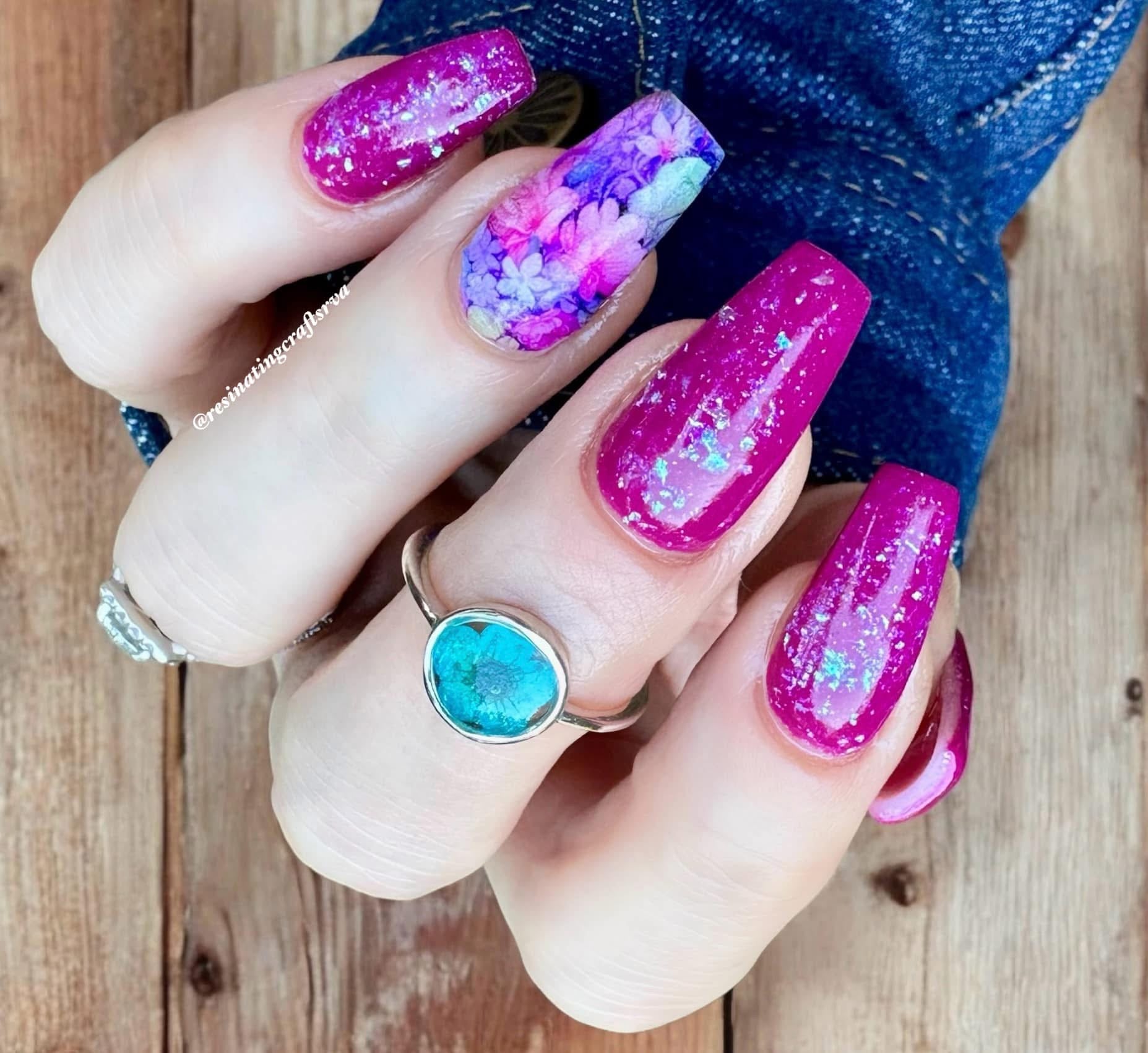 Long acrylic nails with deep purple base and multicolor chamleon flake glitter, accent nail with purple flower design.