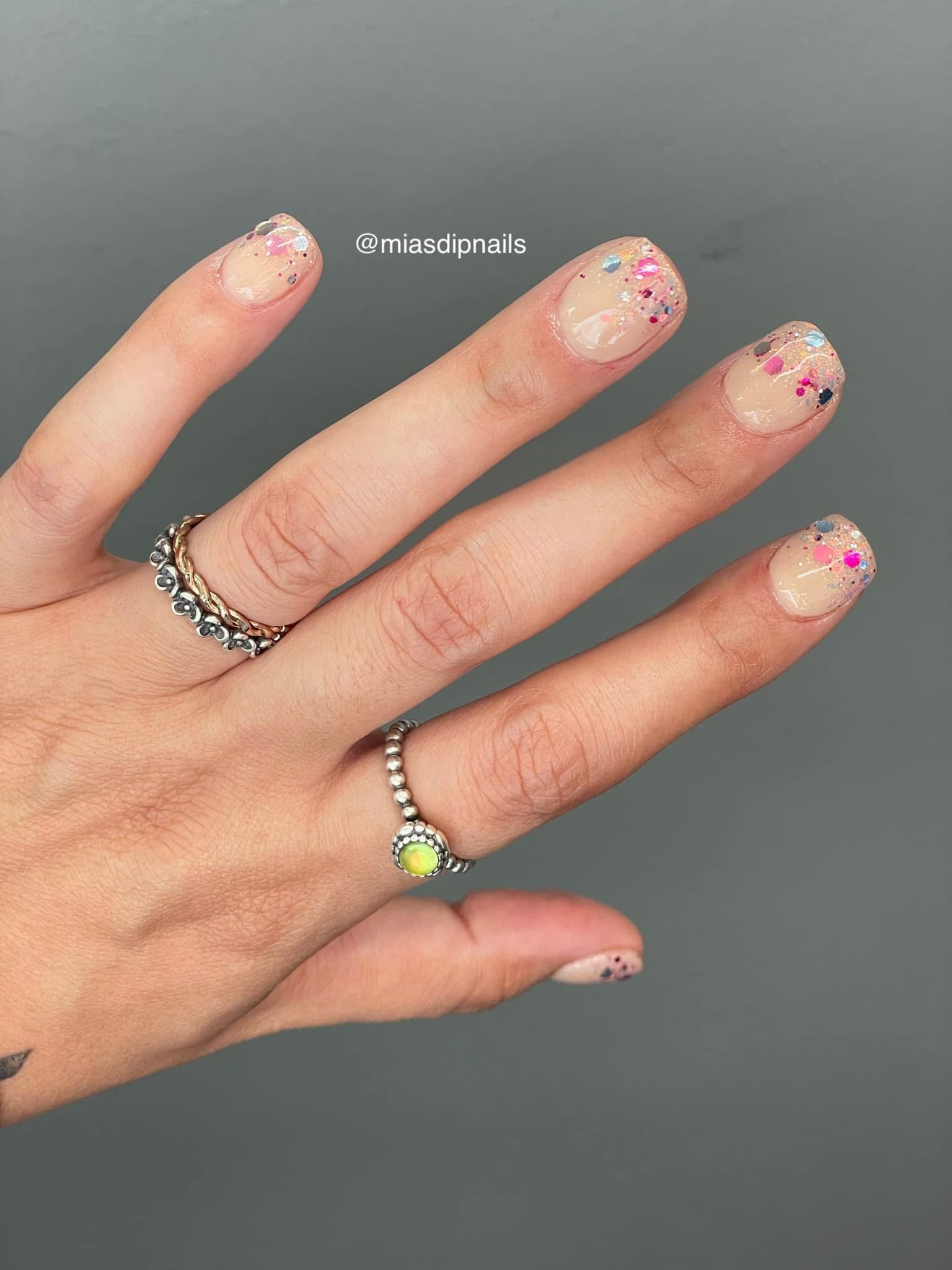 Nude nails with small multicolored confetti dots on natural-shaped tips.