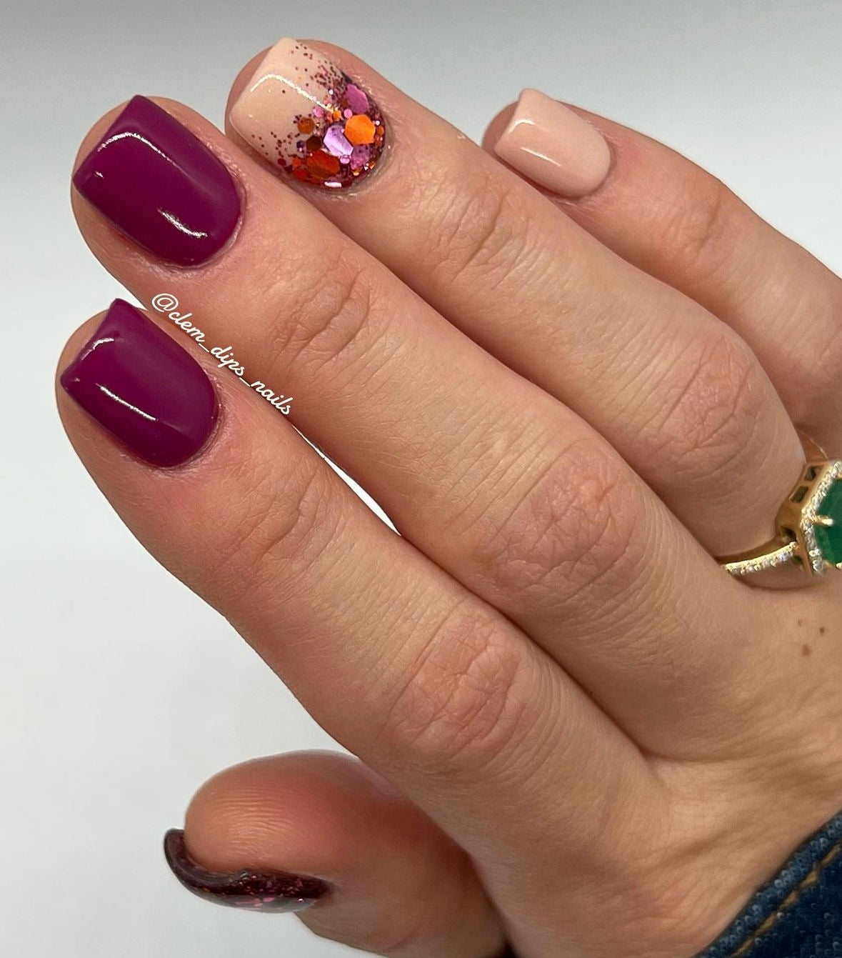 Glossy deep sangria red dip powder nails with a nude accent nail featuring multicolored floral nail art.