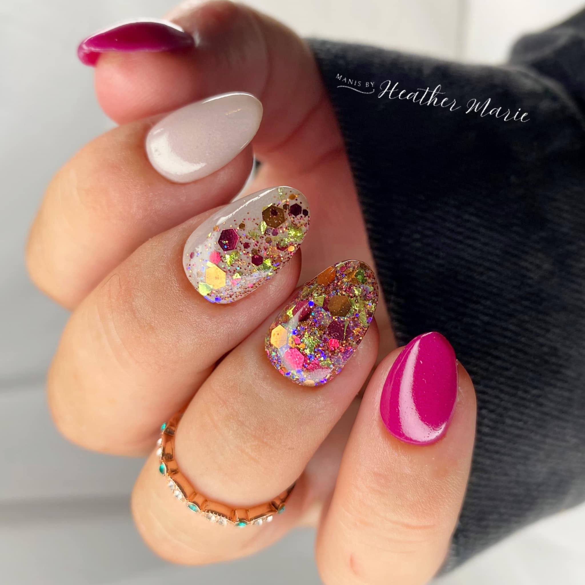 Hand with almond-shaped nails in beige, bright pink, and glittery multicolor designs with gold accents.