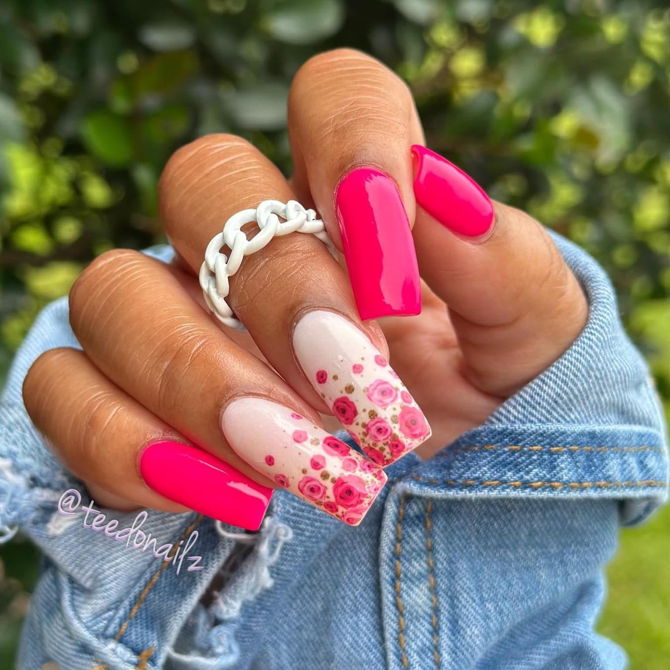 Bright neon pink nails with accent nails featuring pink floral designs and small rhinestones.