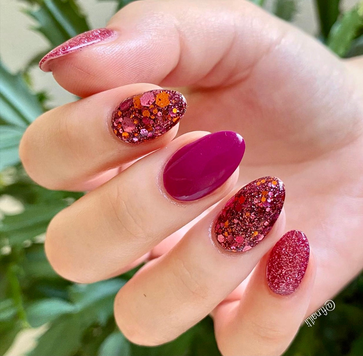 Pink and rose gold glitter and solid plum dip powder nails in almond shape on hand.
