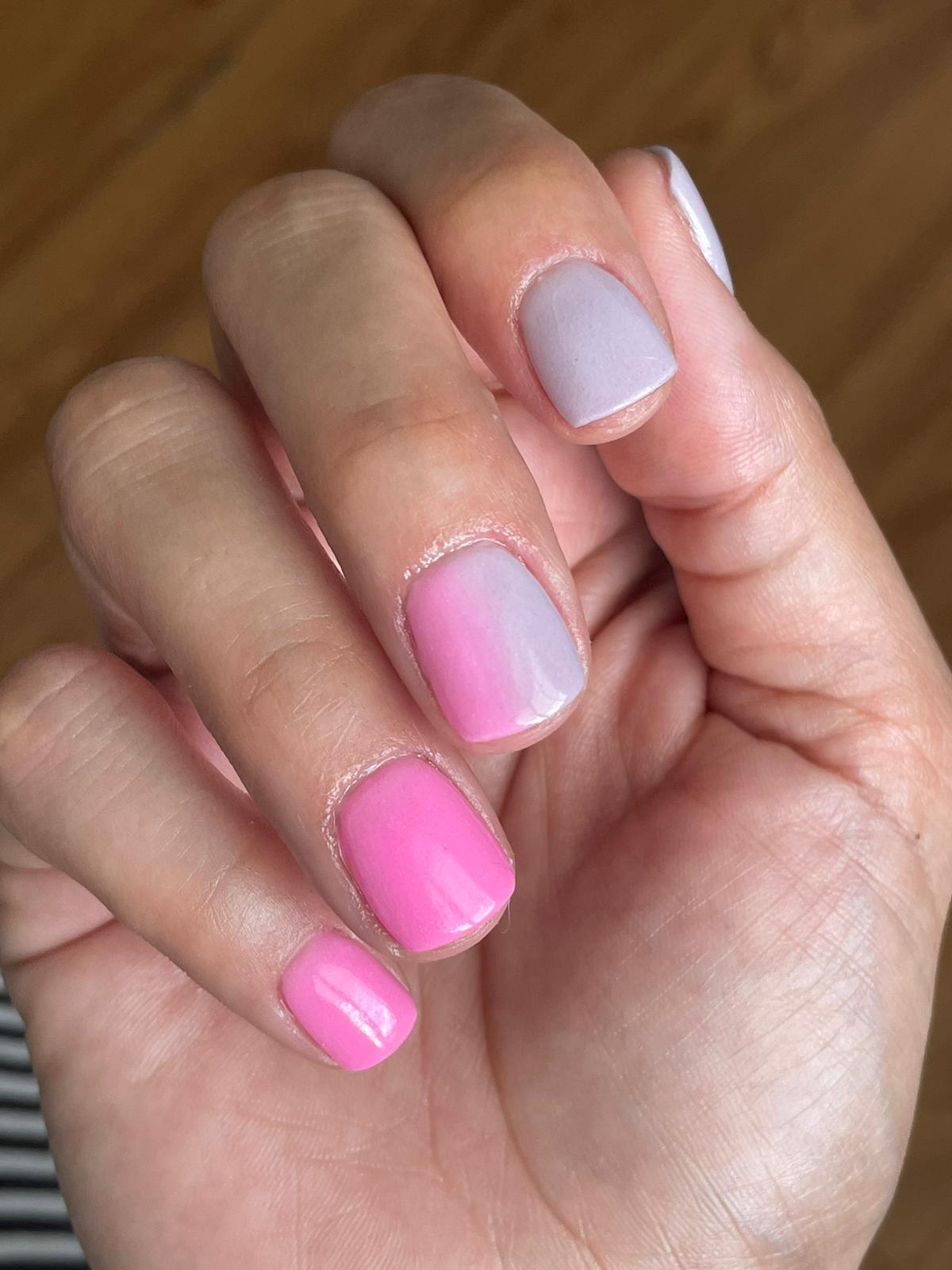 Hand with nails painted in gradient purple shades, from light lilac to bright pink, matte finish.