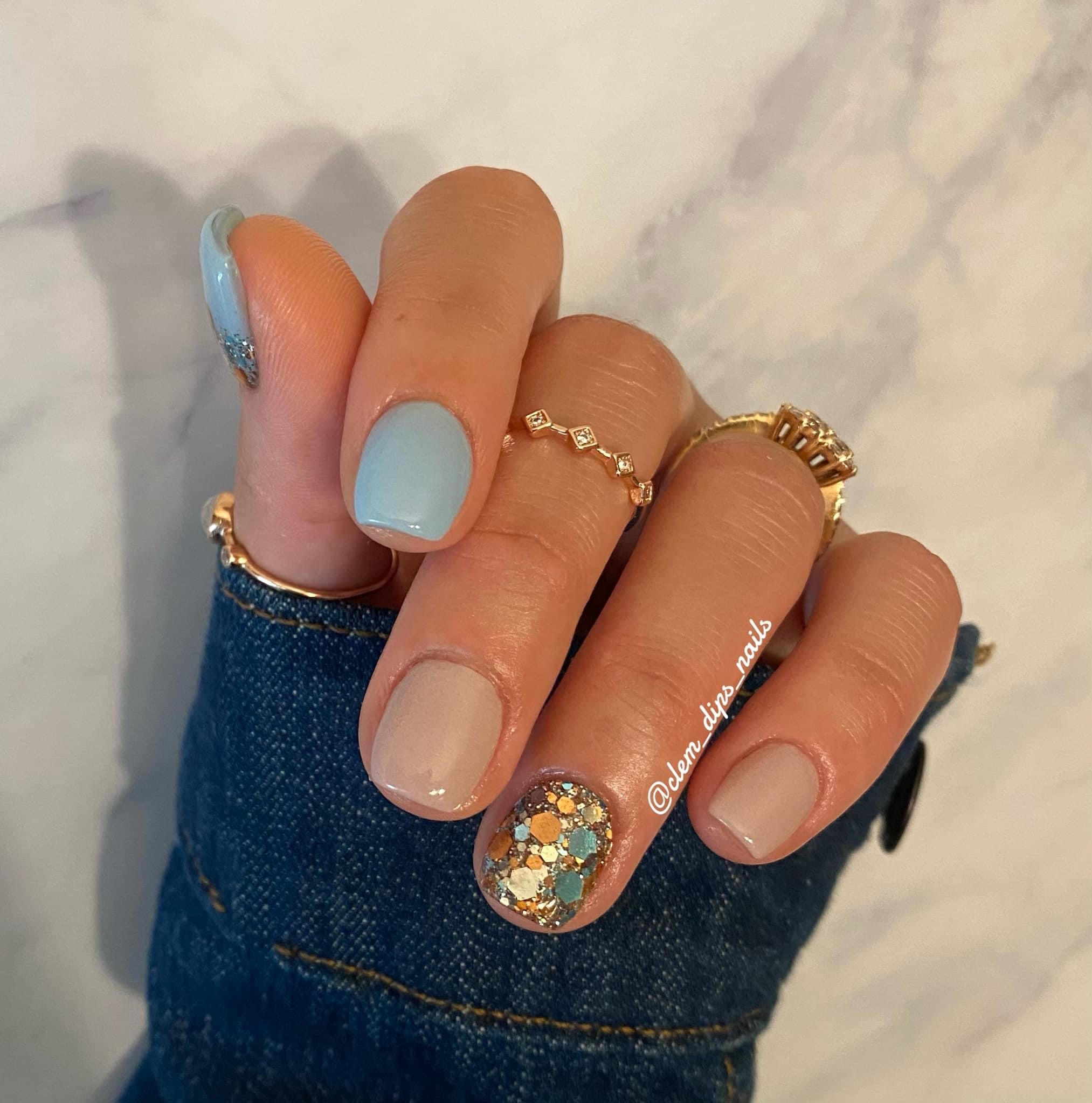 Mix of pastel blue and nude nails with chunky multicolor glitter accent on ring finger.