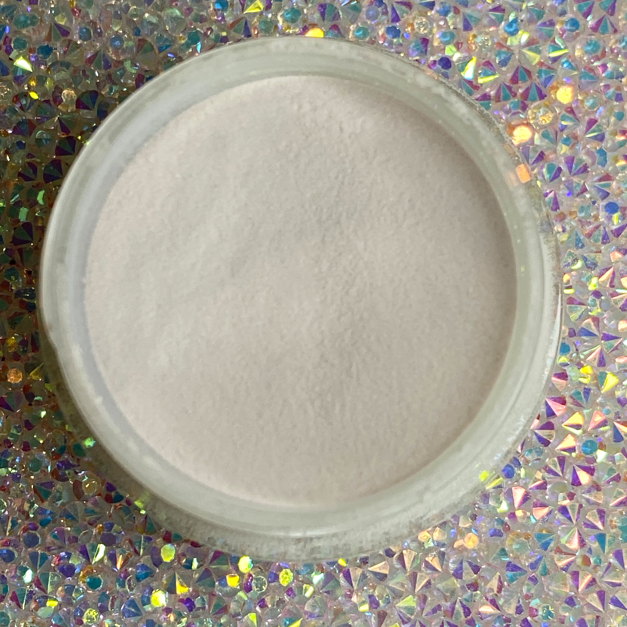 Open jar of fine beige dip powder nail polish on holographic background.