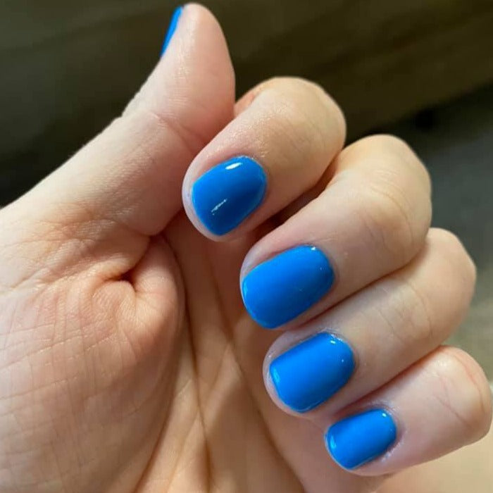 Bright neon electric blue short nails with glossy finish on natural hand.