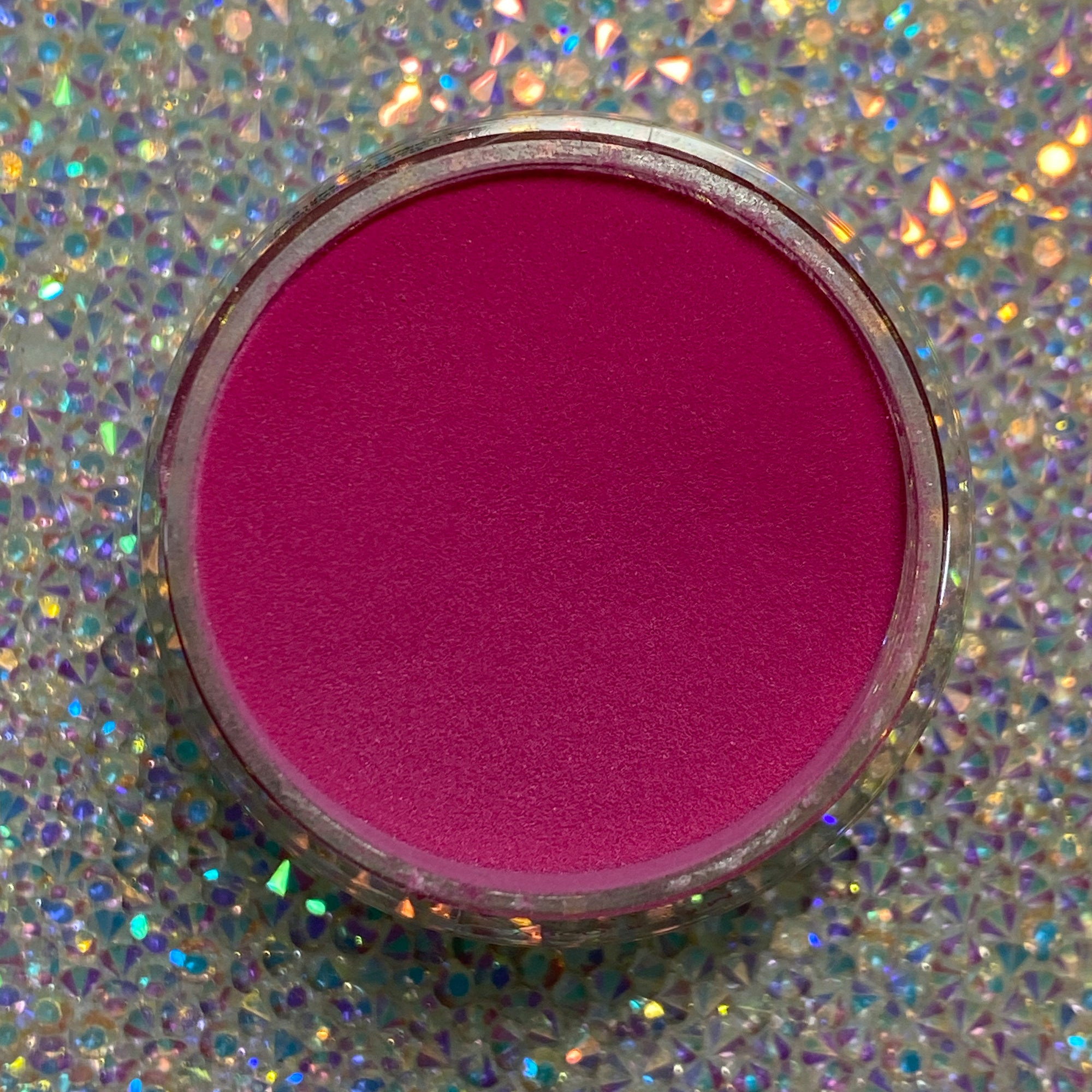 Bright hot pink dip powder in round clear container on holographic surface.