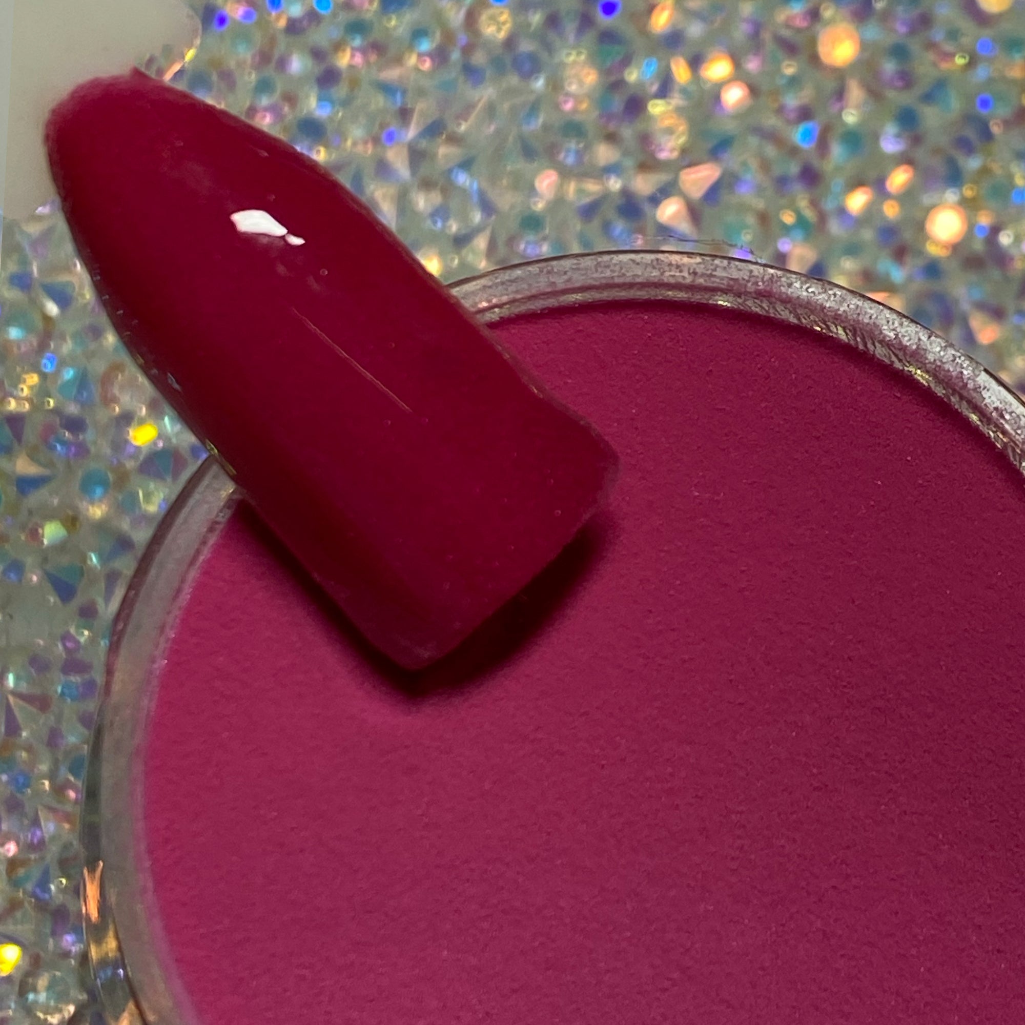 Glossy hot pink nail dip powder swatch over open container with glittery background.