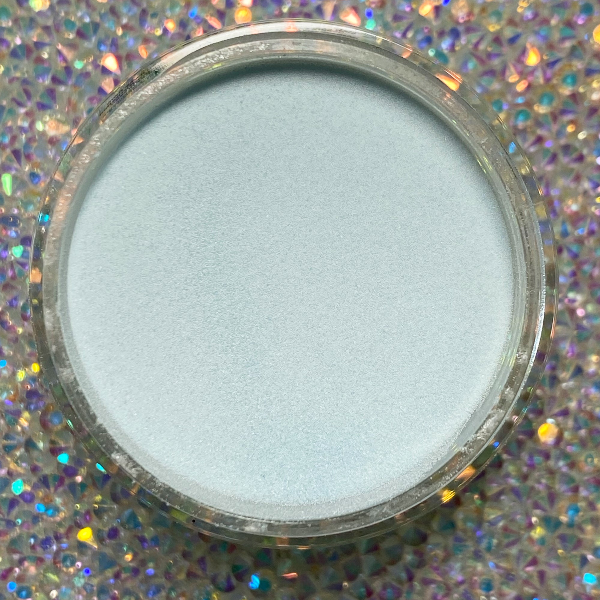 Small jar of light blue dip powder with a smooth, matte finish on a holographic background.