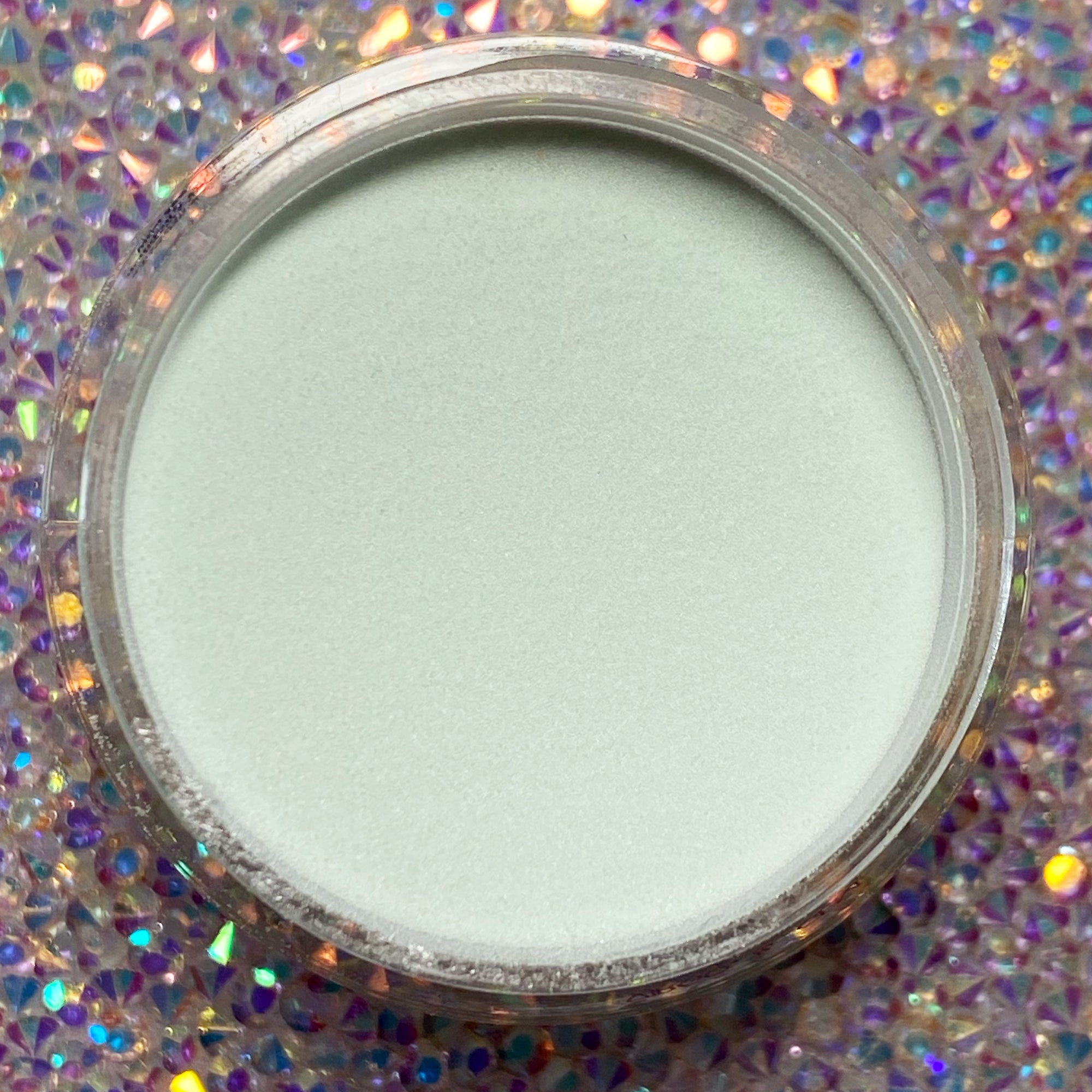 Mint green dip powder in a round clear container on a sparkling iridescent background.
