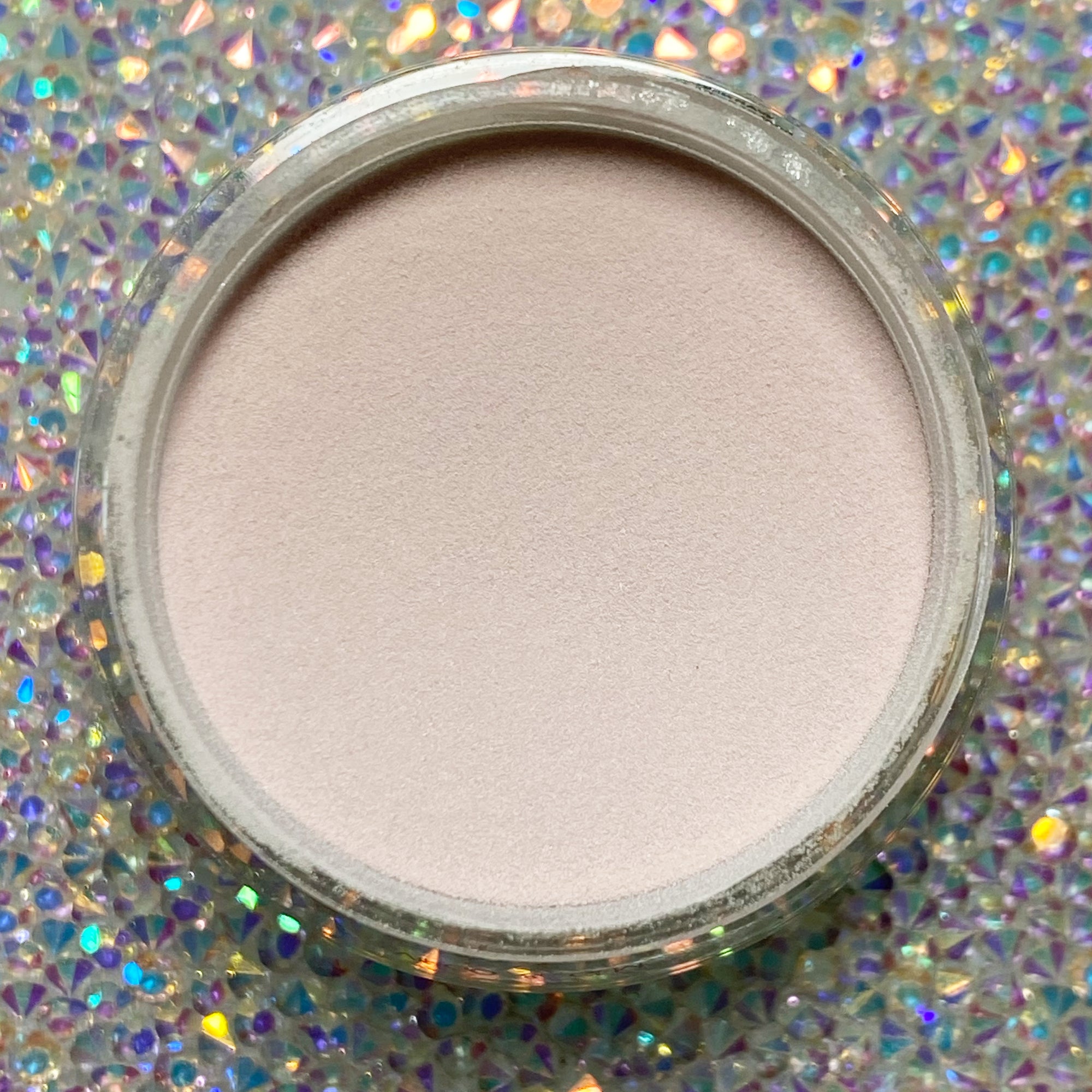 Open jar of pale beige nude dip powder with smooth surface on holographic background.
