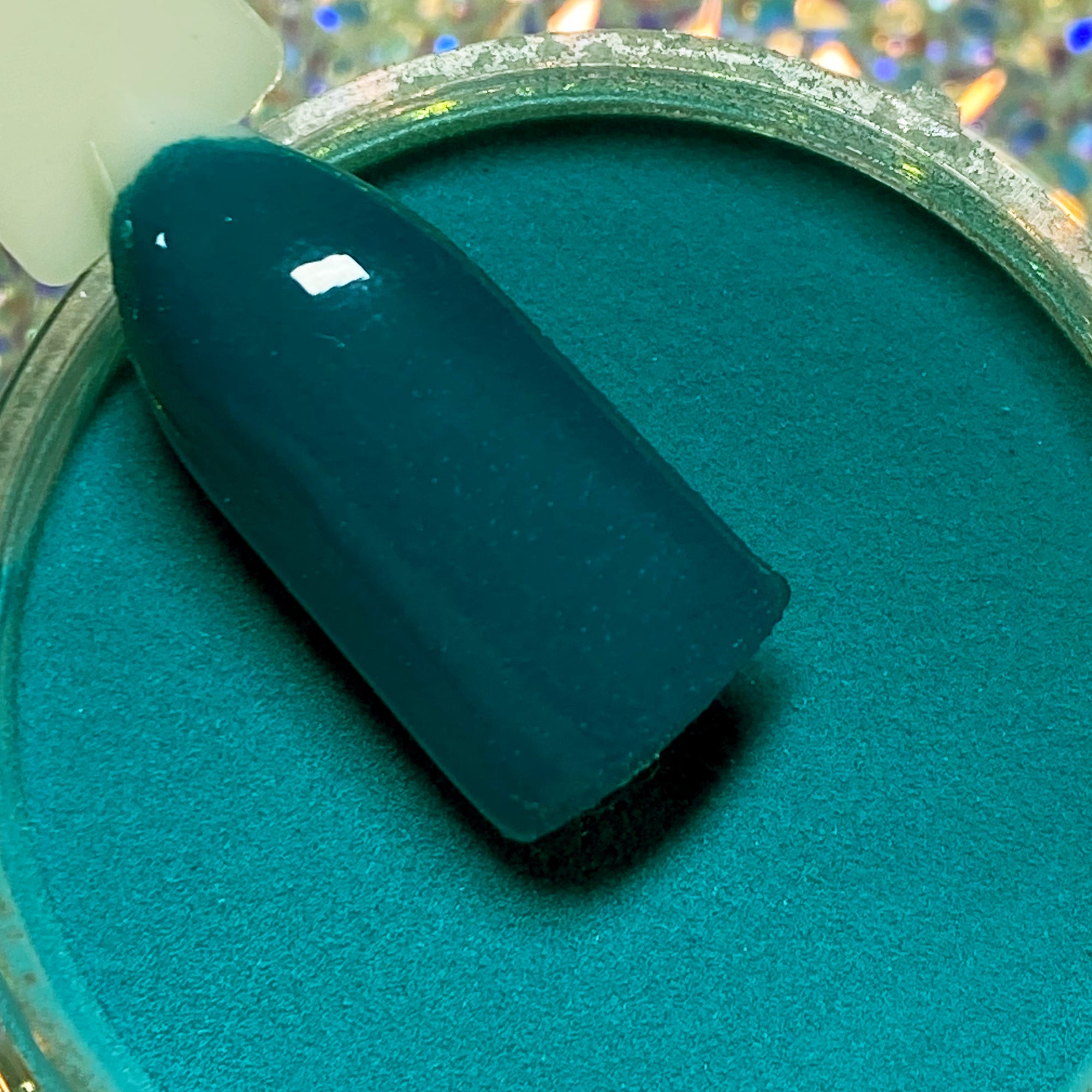 Teal-green glossy nail tip resting on matching dip powder pot labeled DP132 Rio.