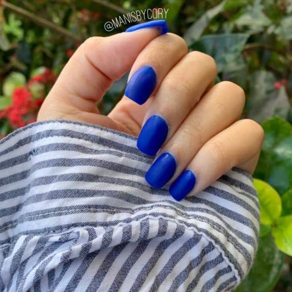Matte royal blue dip powder nails on natural hand with striped gray and white sleeve background.