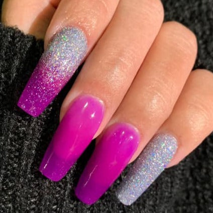 Long nails with a holographic silver glitter on thumb, index, and pinky, fading to bright purple ombre on middle and ring.