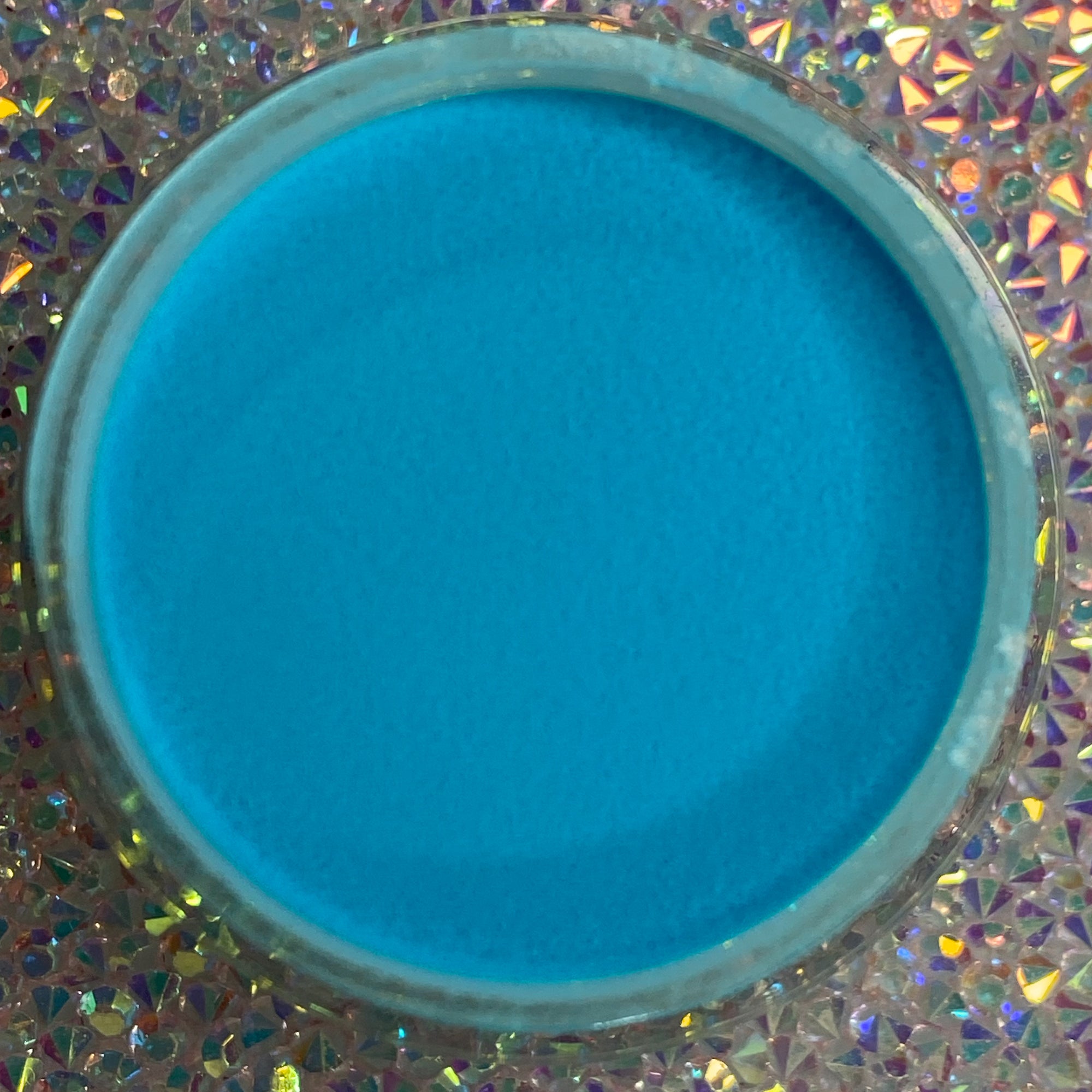 Bright neon blue dip powder in a round container on a holographic surface.