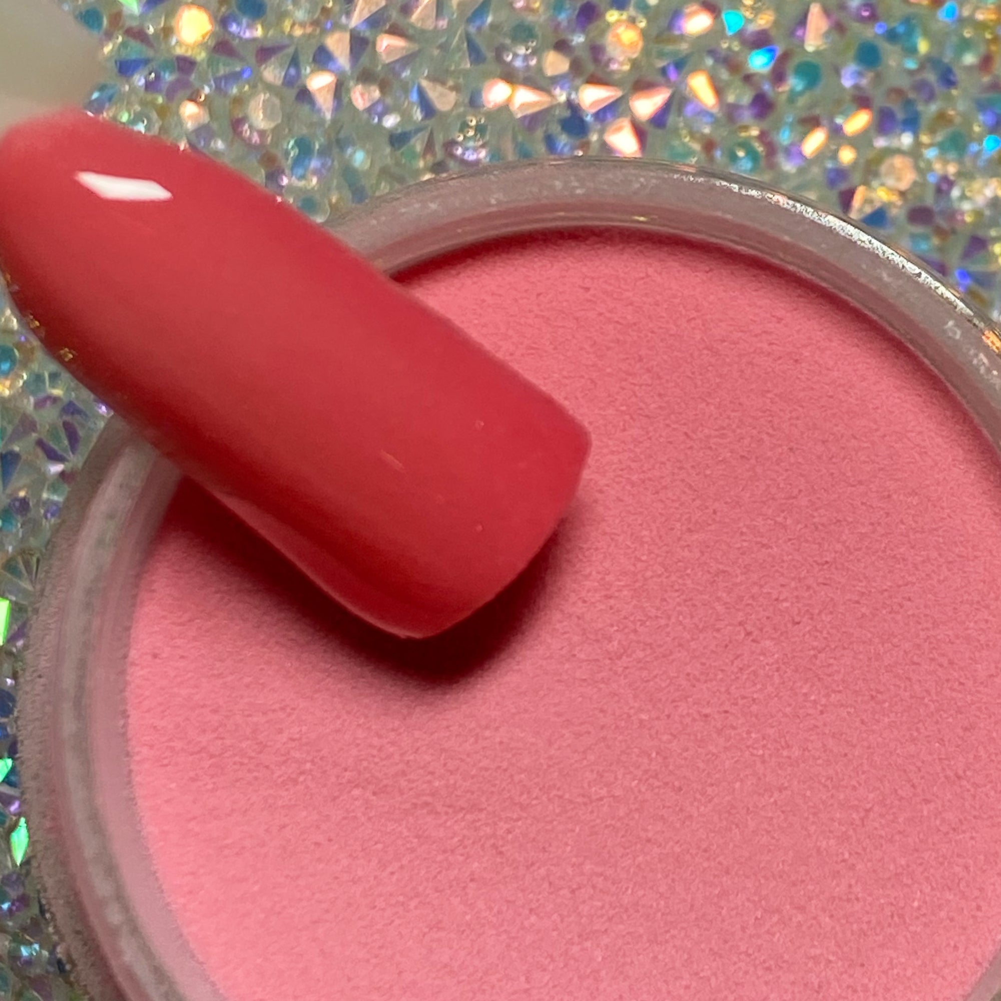 Bright pink dip powder with smooth matte finish on nail tip over open container on holographic background.