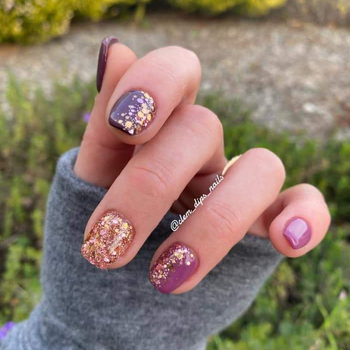 Manicure with deep mauve and rose gold chunky glitter nails on natural hands outdoors.