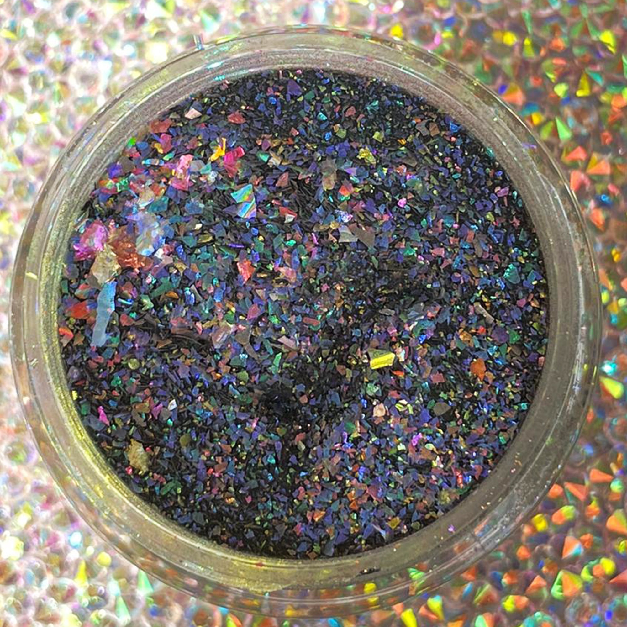 Small jar of black dip powder with multicolor chameleon flakes reflecting purple, blue, green, and orange hues.