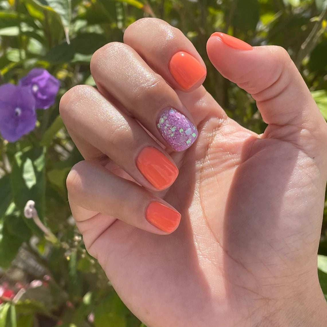 Bright peach-orange nails with a glittery lavender accent nail on natural hand.