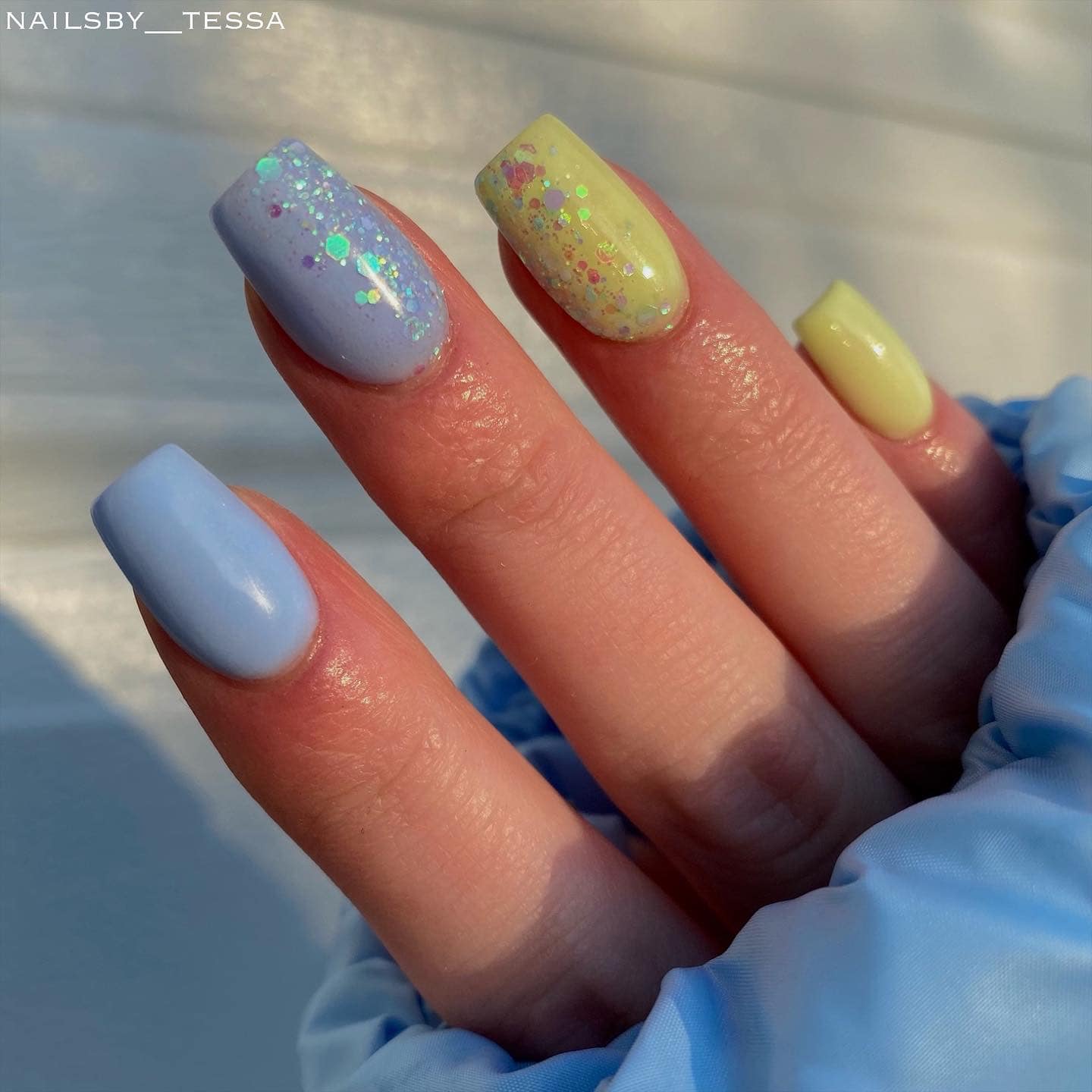 Long square nails with pastel blue and yellow dip powder, decorated with green and yellow glitter accents.