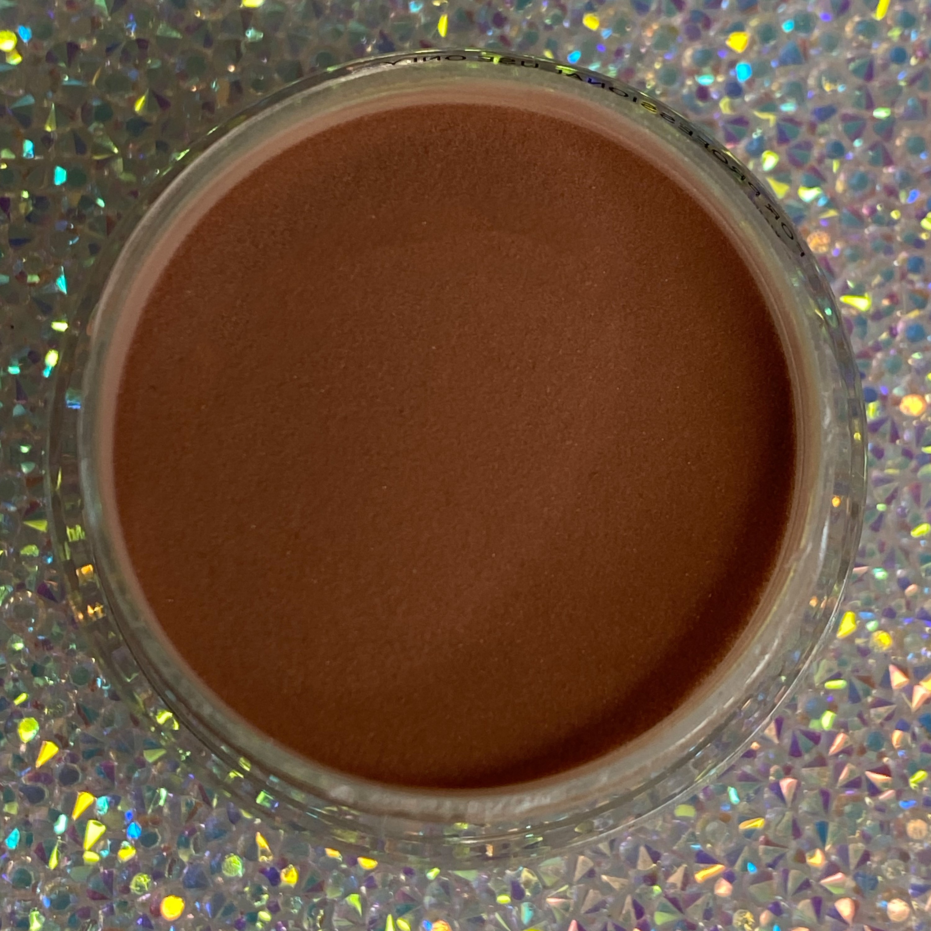 Open jar of smooth, warm medium brown dip powder on holographic surface.