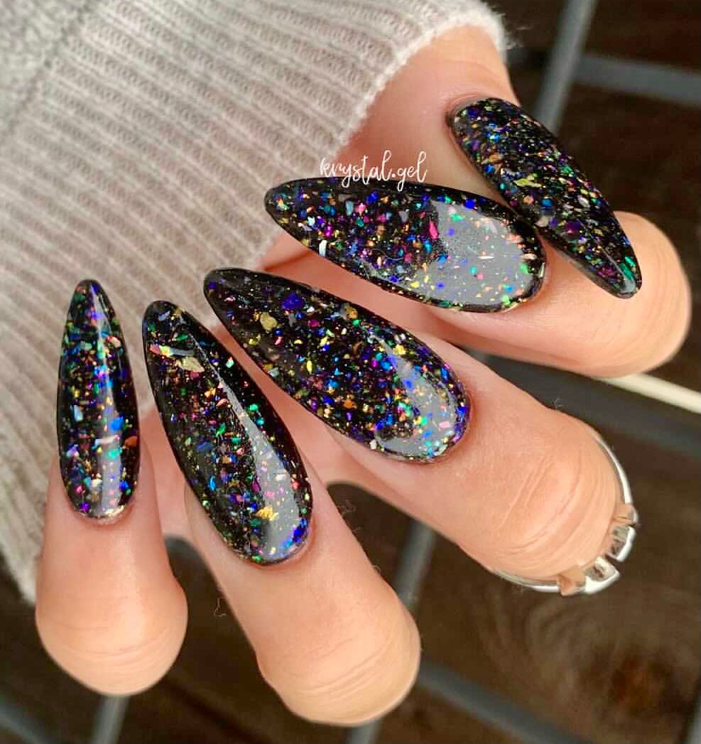Long almond-shaped nails with black base and multicolor chameleon flake dip powder design.