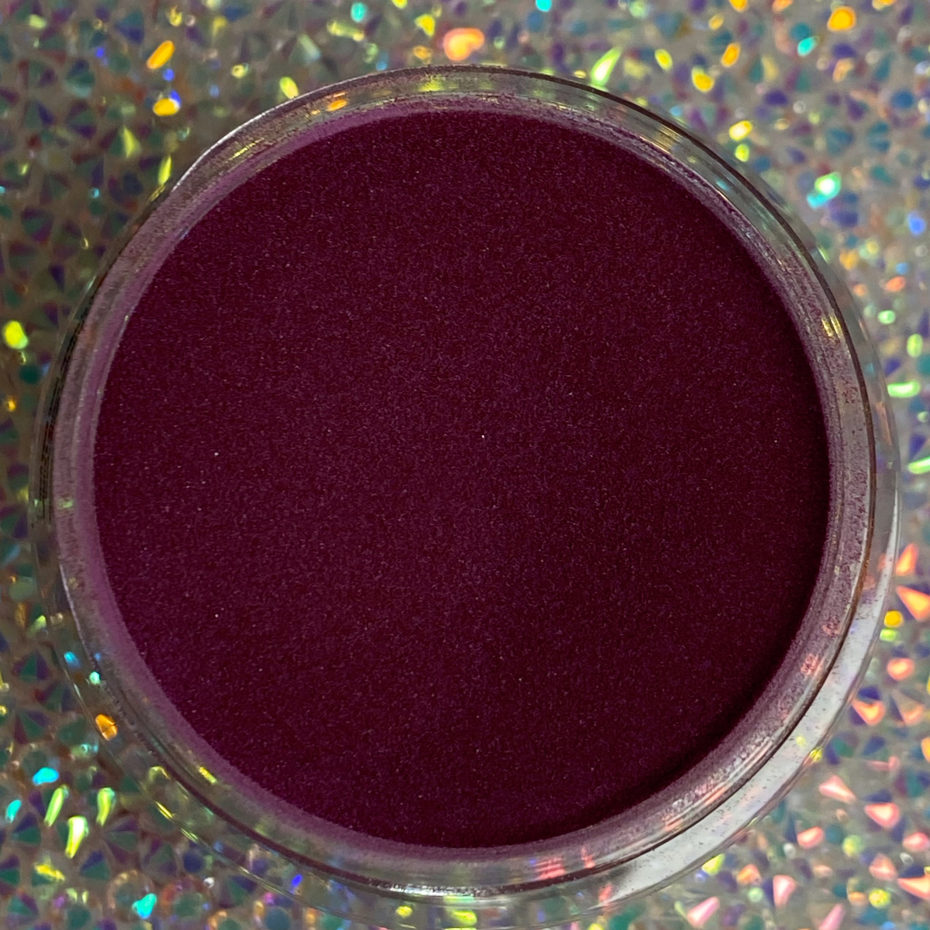 Deep wine-red dip powder in clear round container with holographic background.