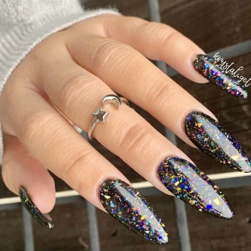 Long almond-shaped nails with black chameleon flake dip powder featuring multicolor reflective flakes.