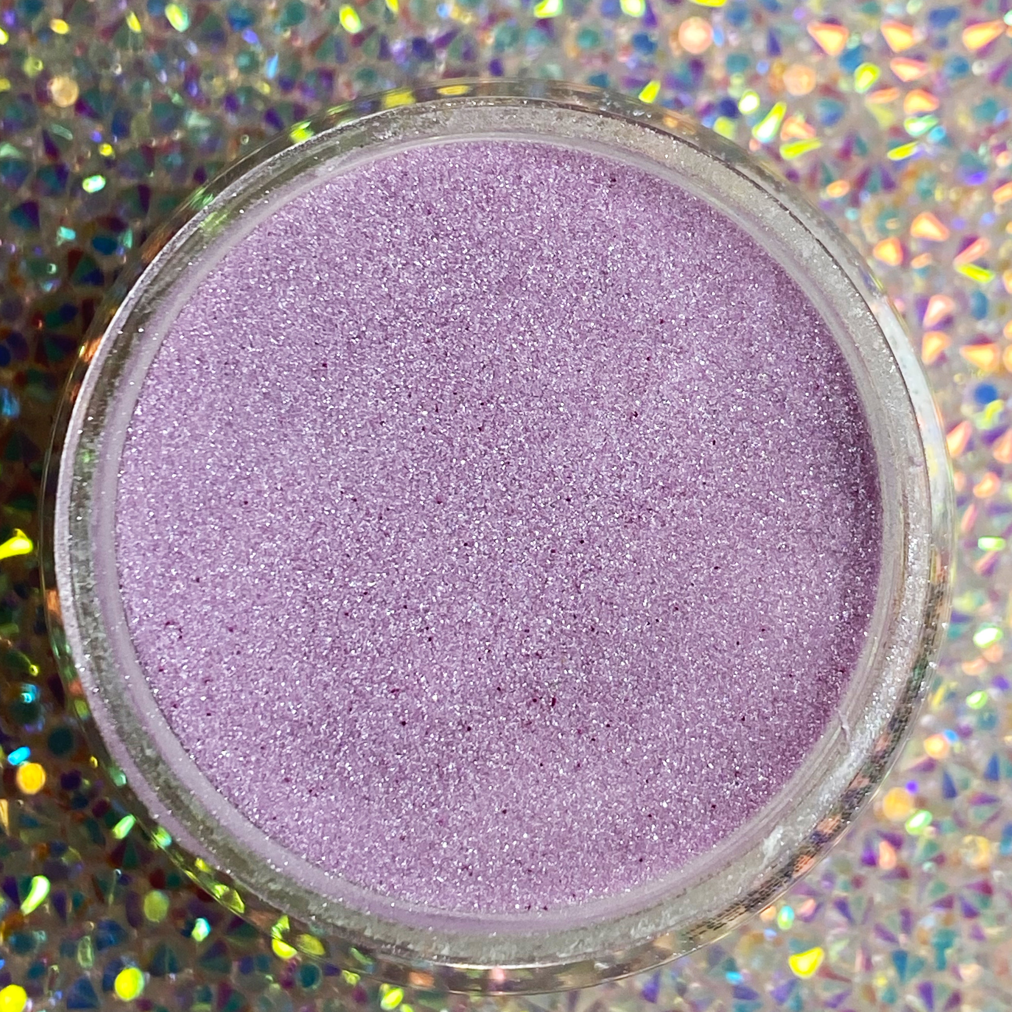 Open jar of fine purple shimmer glitter dip powder on holographic background.