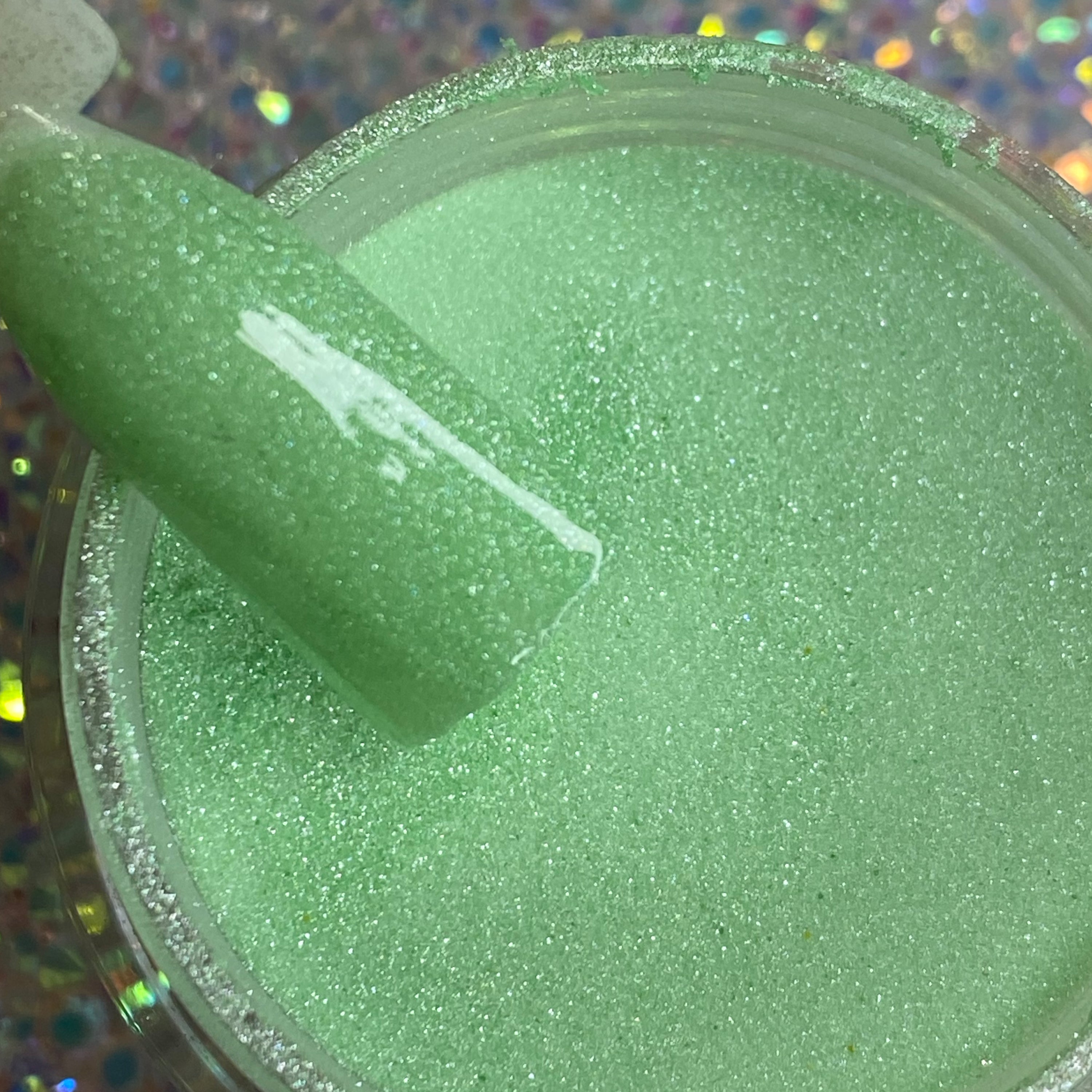 Open jar of mint green glitter dip powder with a swatch stick showing fine shimmer.
