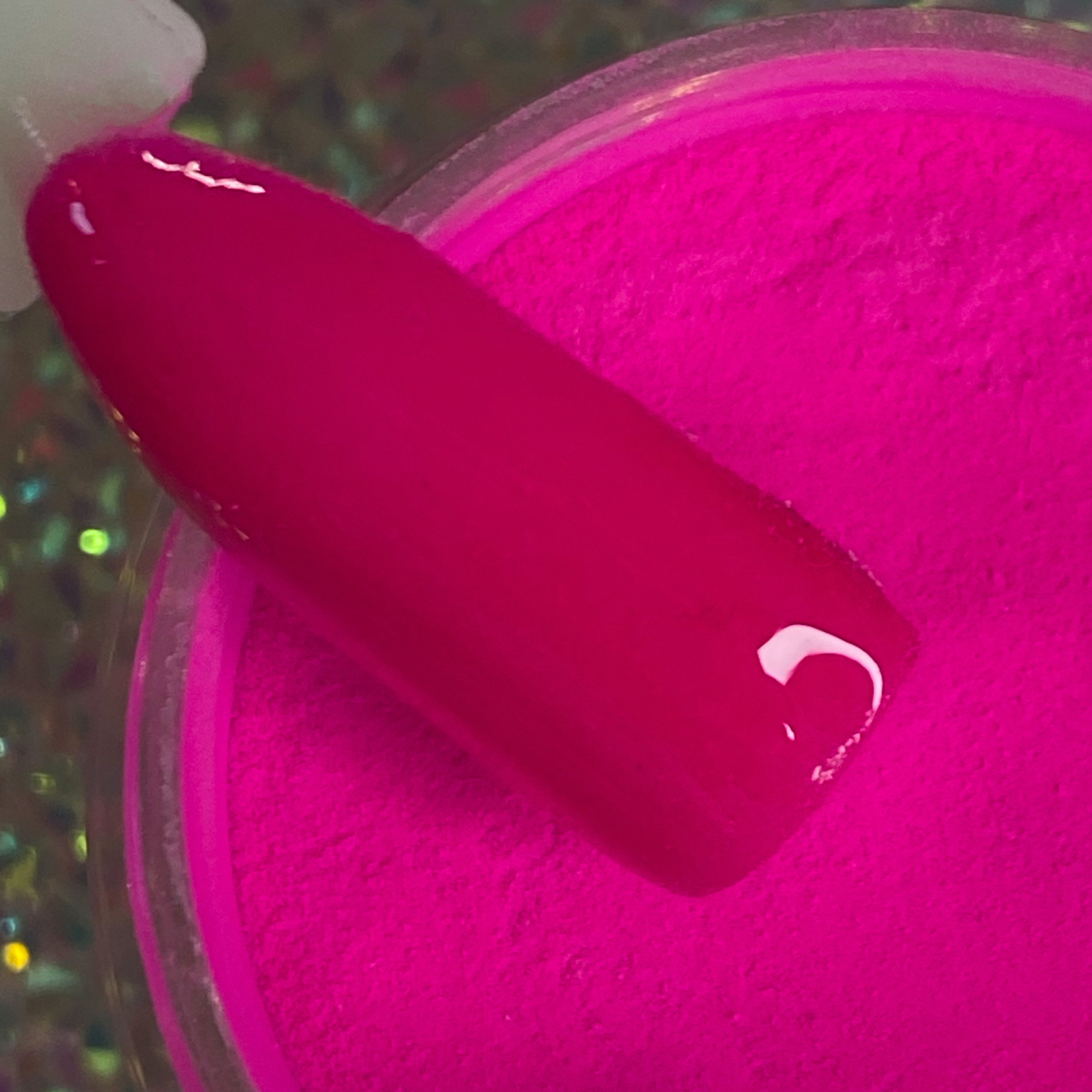 Bright neon pink dip powder with glossy finish on nail tip over open container.