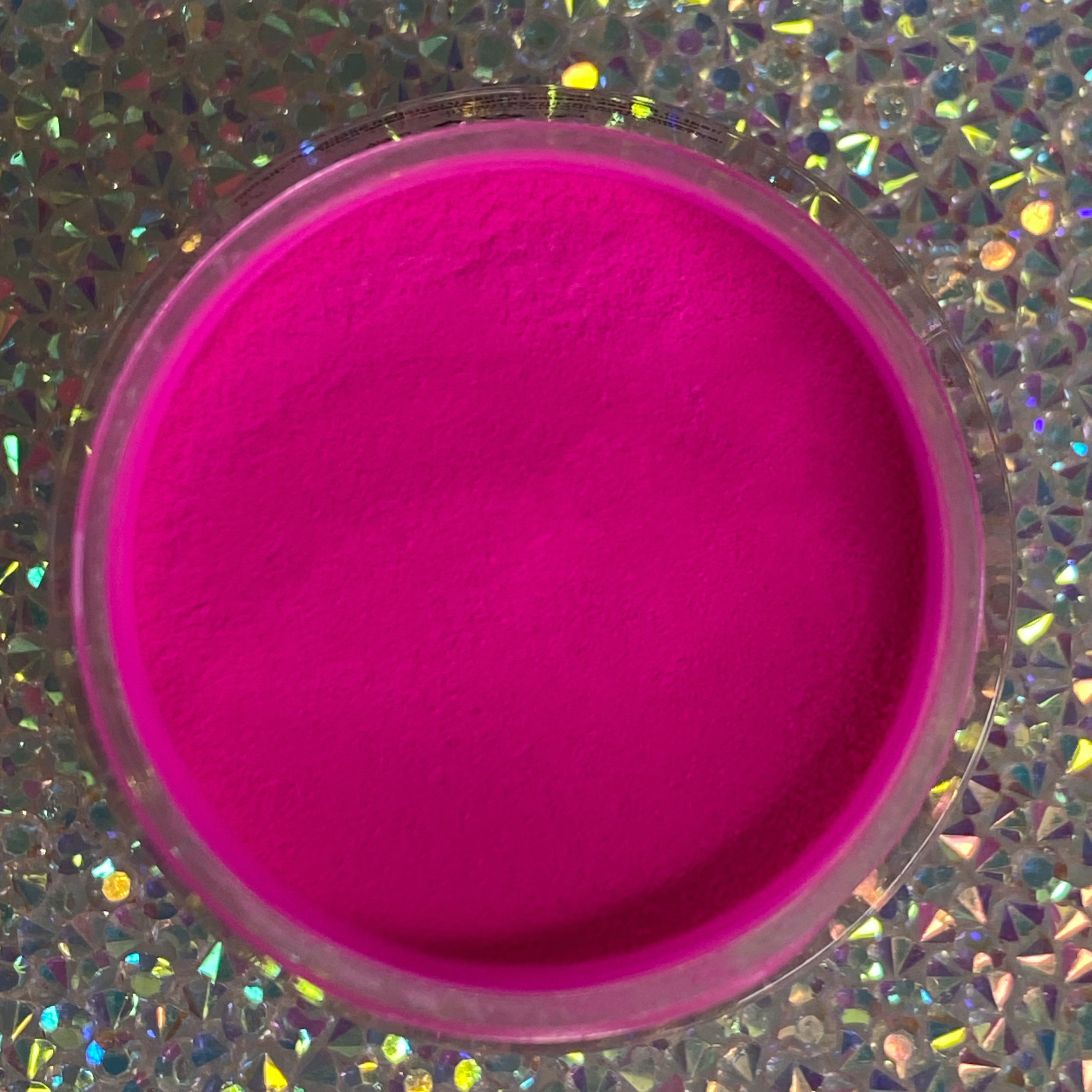 Bright neon pink glow-in-the-dark dip powder in a clear round container on a holographic surface.