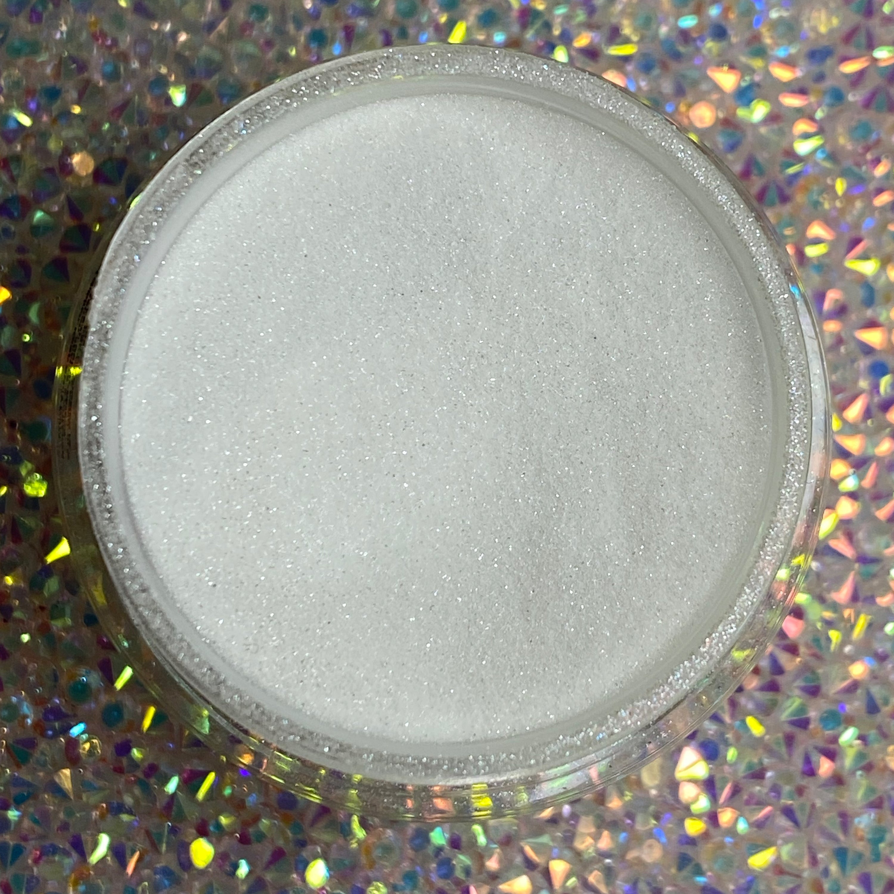 Fine white dip powder with subtle shimmer in a clear round jar on a holographic glitter background.
