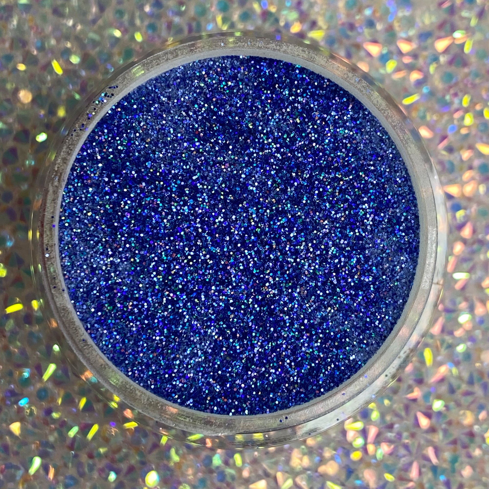 Bright holographic blue fine glitter powder in a round clear container.