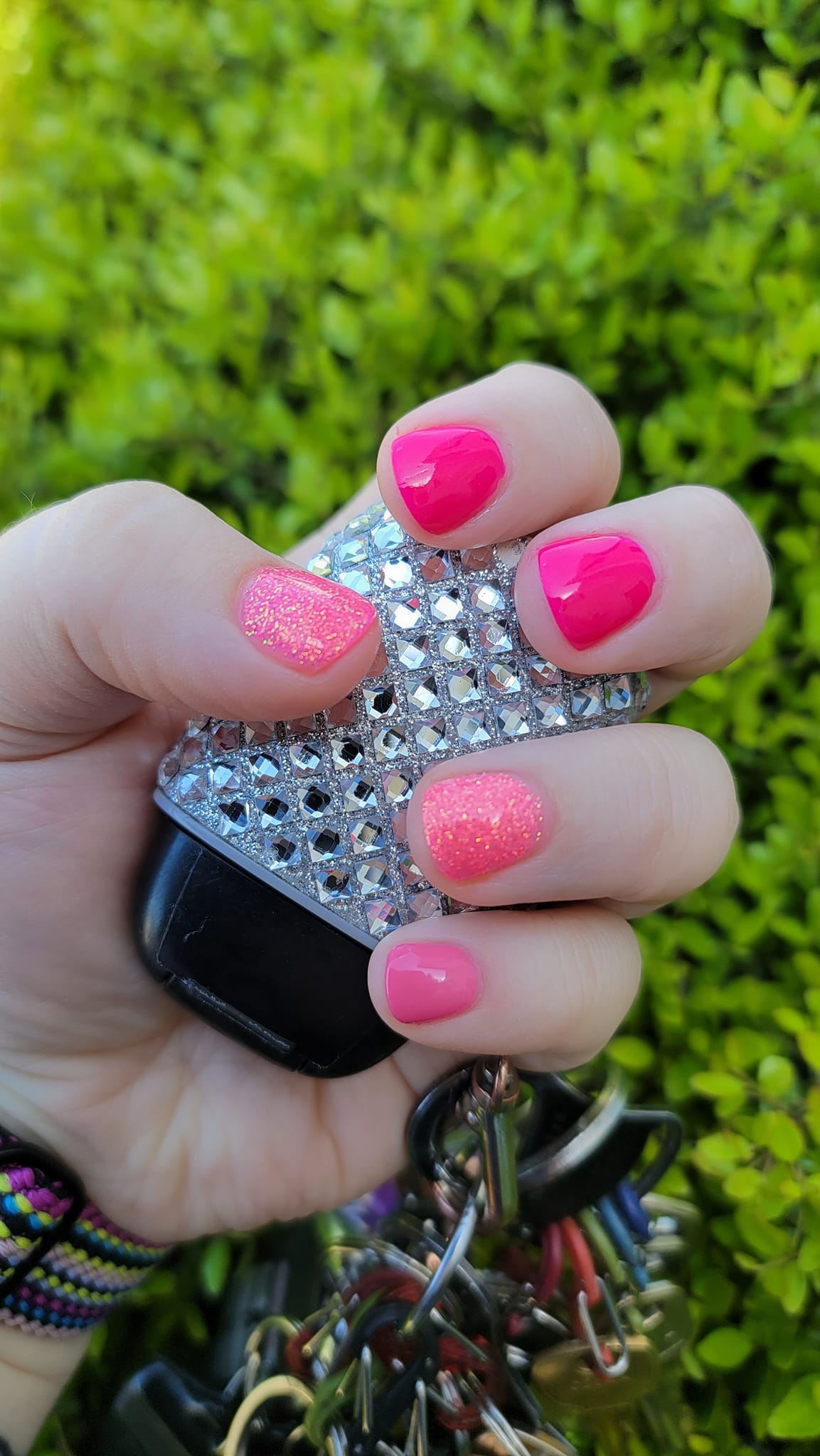 Bright pink and coral dip powder nails with fine iridescent glitter accent on ring finger.