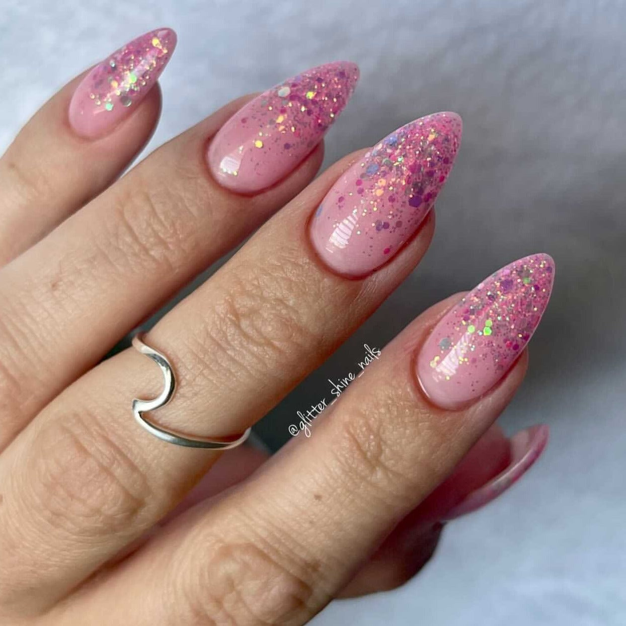 Long almond-shaped nails with pink chunky glitter and multicolor mother of pearl shimmer on a clear base.