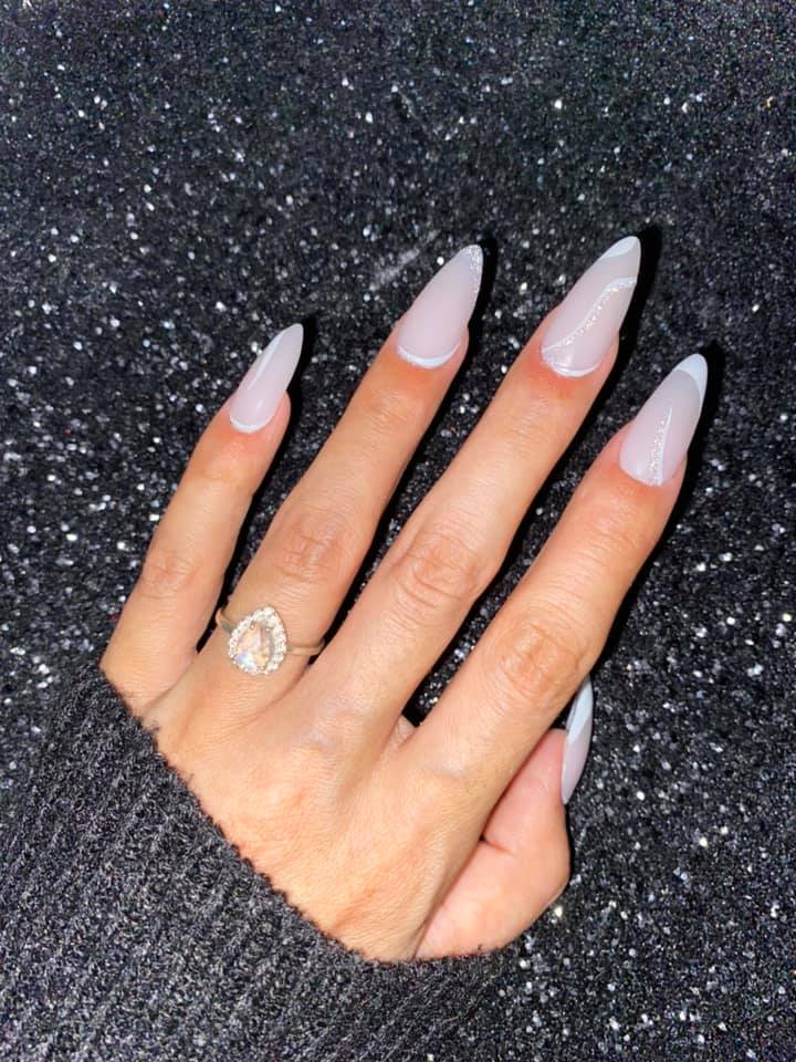 Long almond-shaped nails with smooth, glossy nude beige dip powder polish on a hand wearing a dark gray sweater against a.